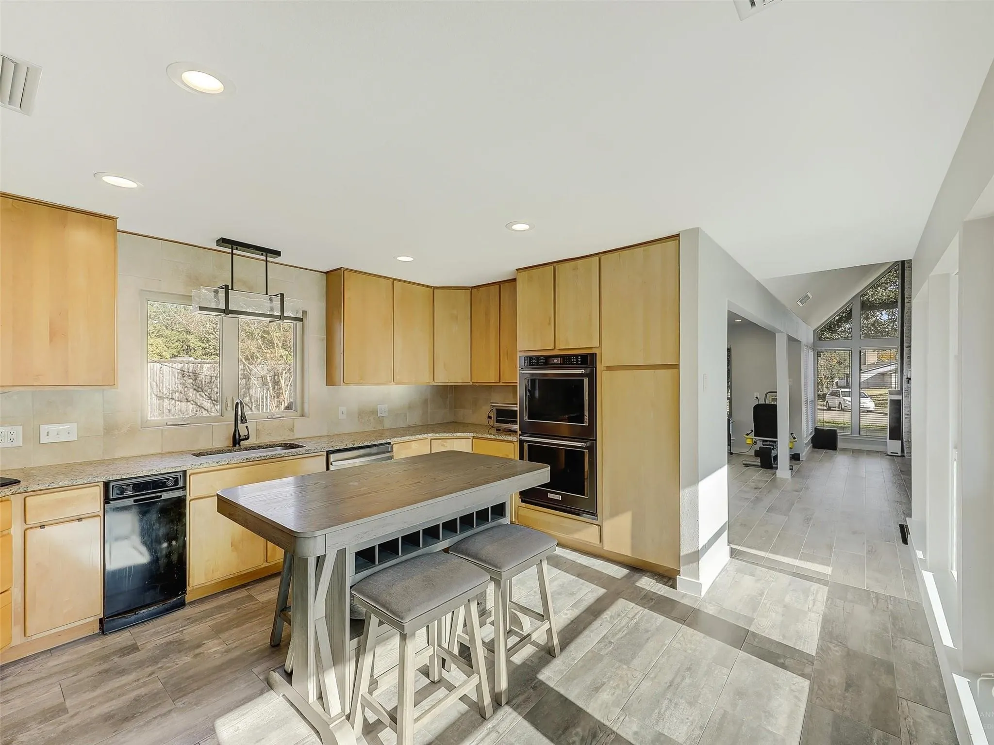 Kitchen with black double oven, light hardwood / wood-style flooring, light brown cabinets, stainless steel dishwasher, and sink