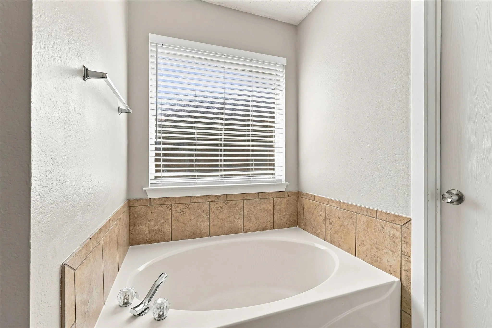 White corner tub with chrome fixtures, complemented by a tiled surround