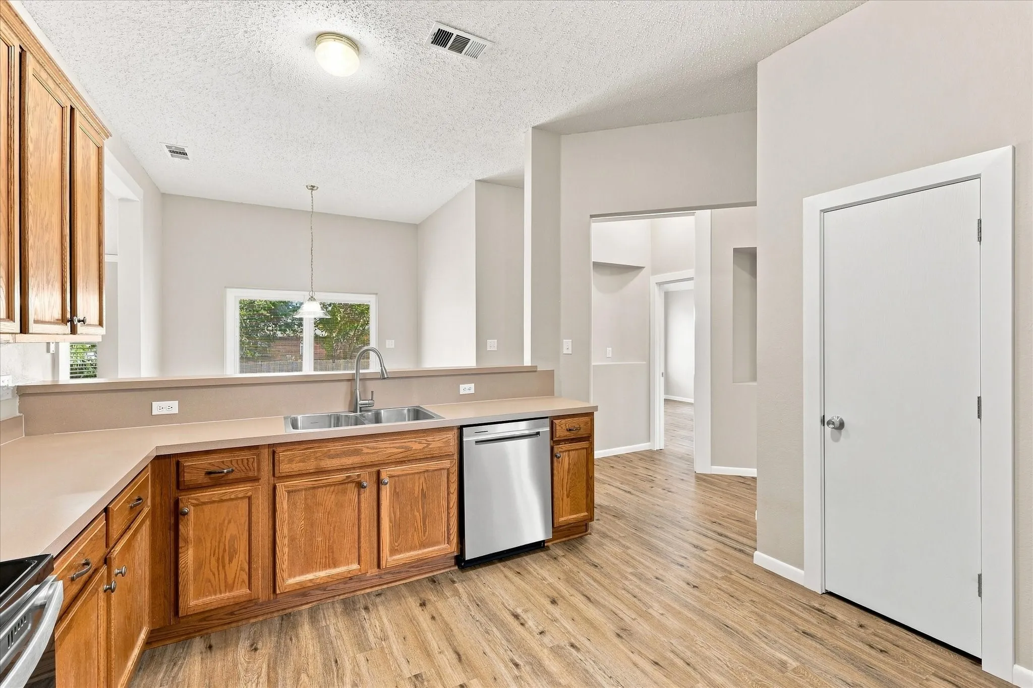 Kitchen featuring wood-finish flooring, wood cabinetry, a stainless steel dishwasher, and a double basin sink with a high-arc faucet