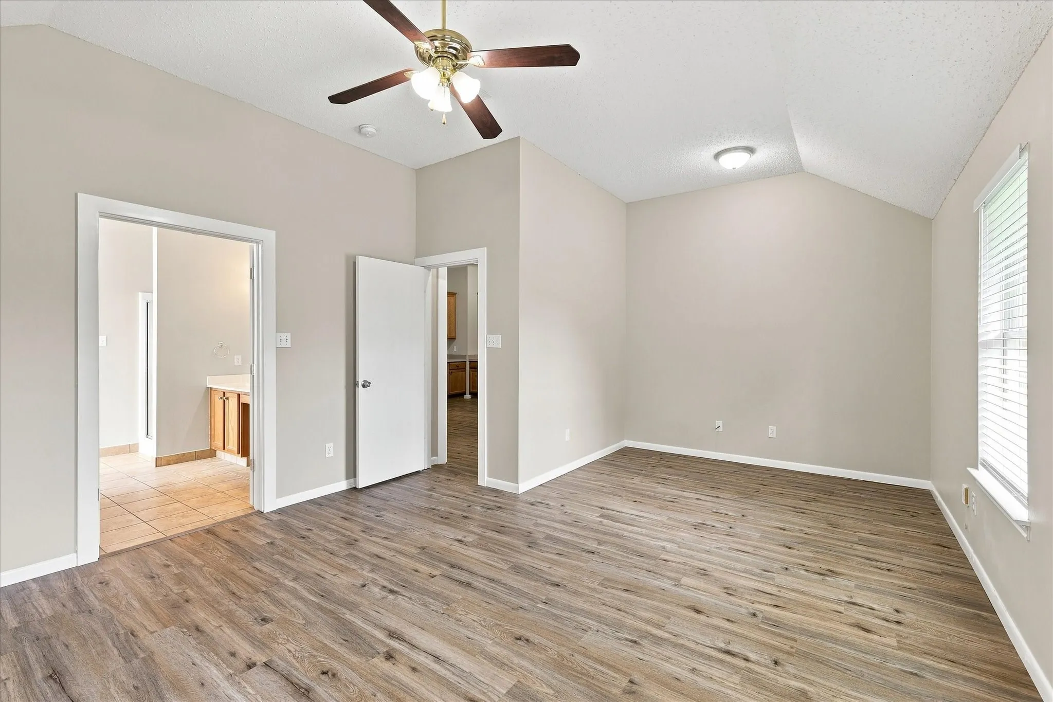Wood-finish flooring, vaulted ceiling, ceiling fan with integrated lighting, recessed lighting, and window with blinds