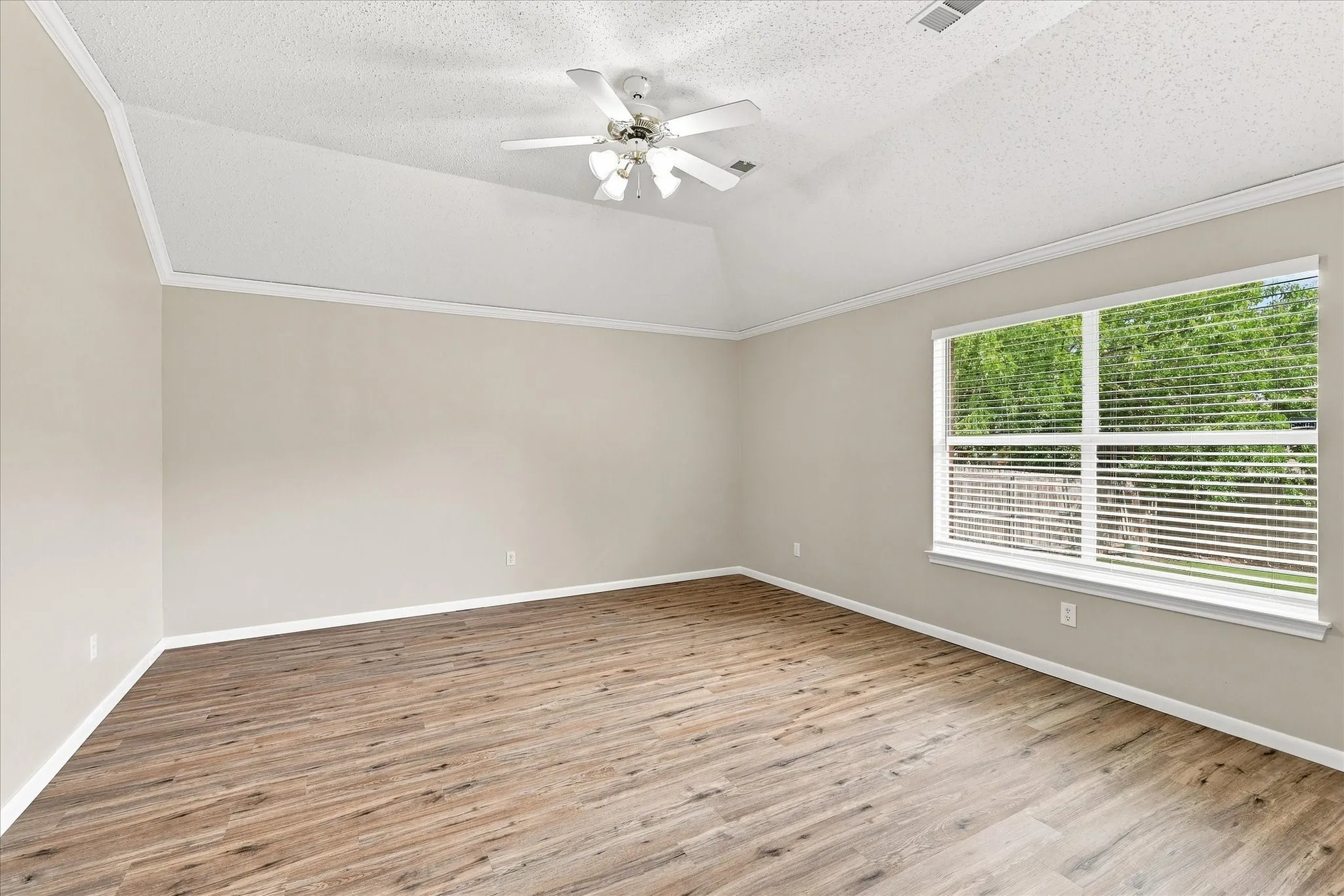 Vaulted ceiling, wood-finish flooring, ceiling fan with light kit, and large window with blinds