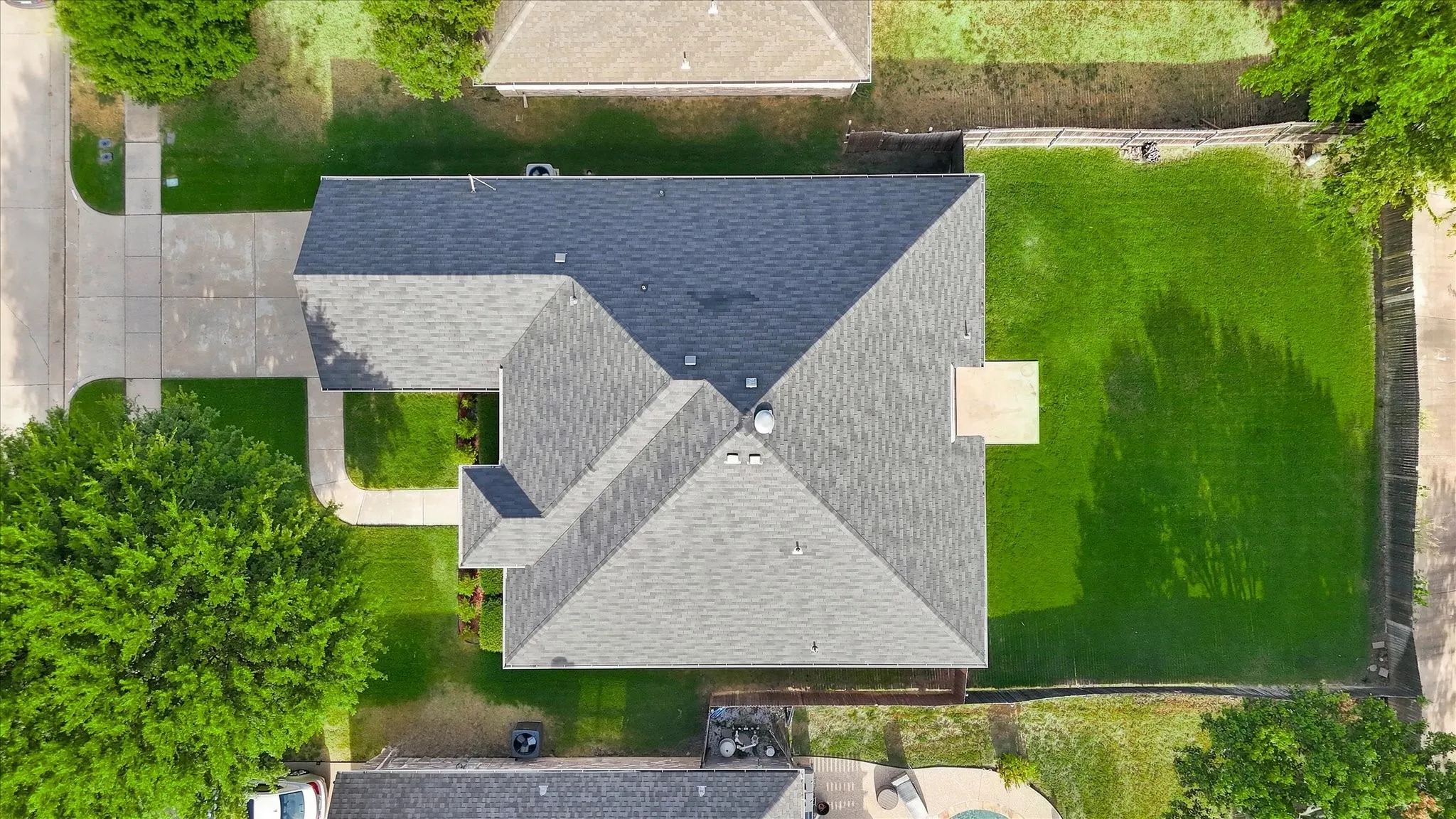 Gabled roofline with dark shingles, expansive green lawn, concrete driveway, and mature perimeter trees