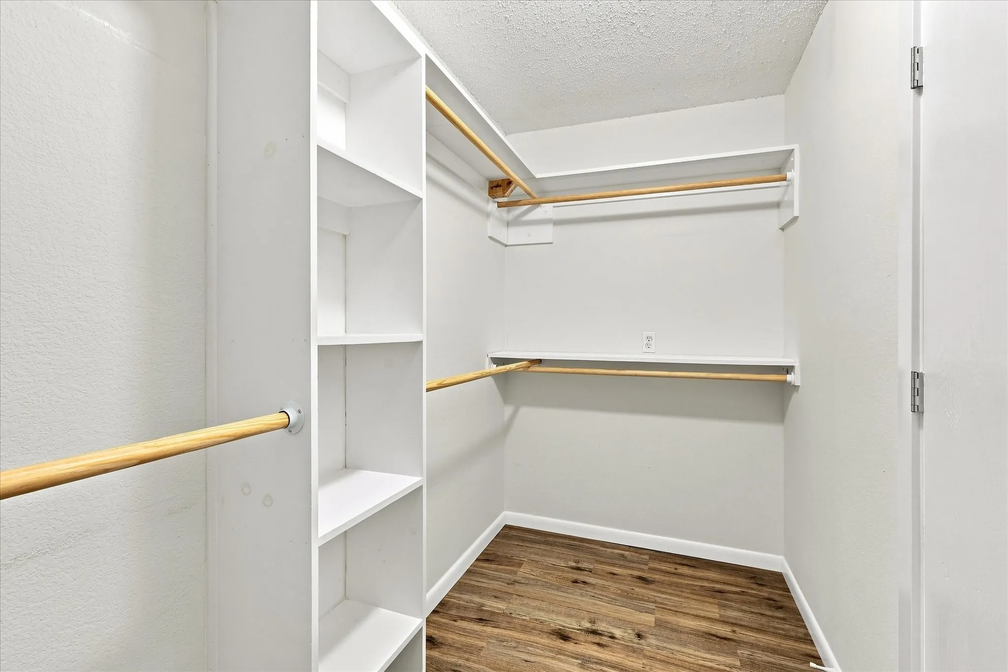 Walk-in closet featuring built-in shelving, multiple hanging rods, and wood-finish flooring