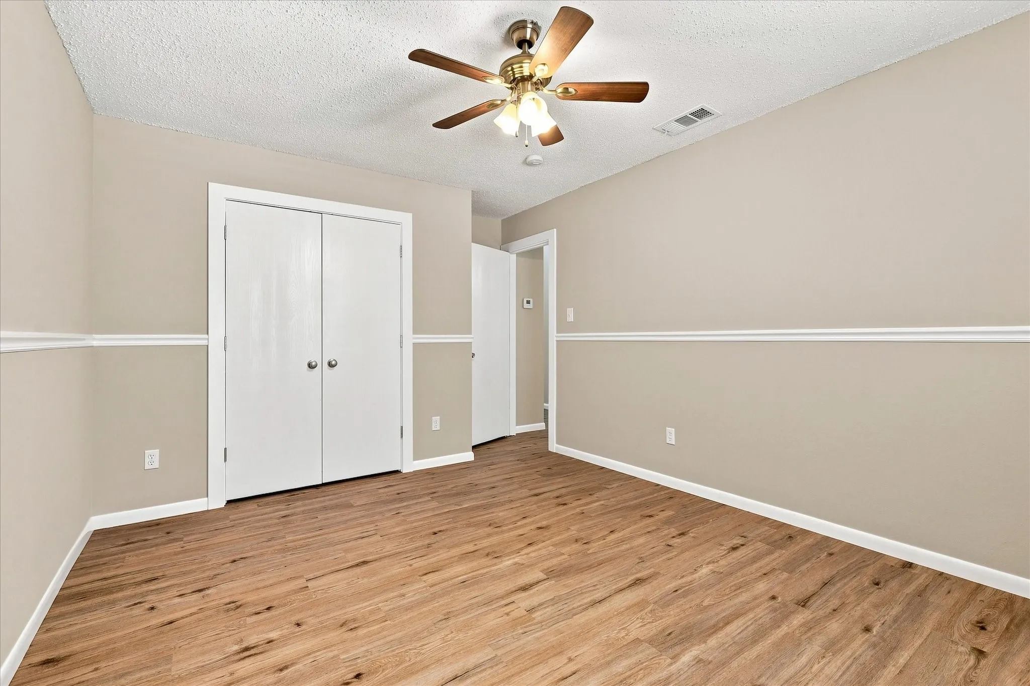 Wood-finish flooring, neutral wall tones, white trim, dual-door closet, and ceiling fan with integrated lighting
