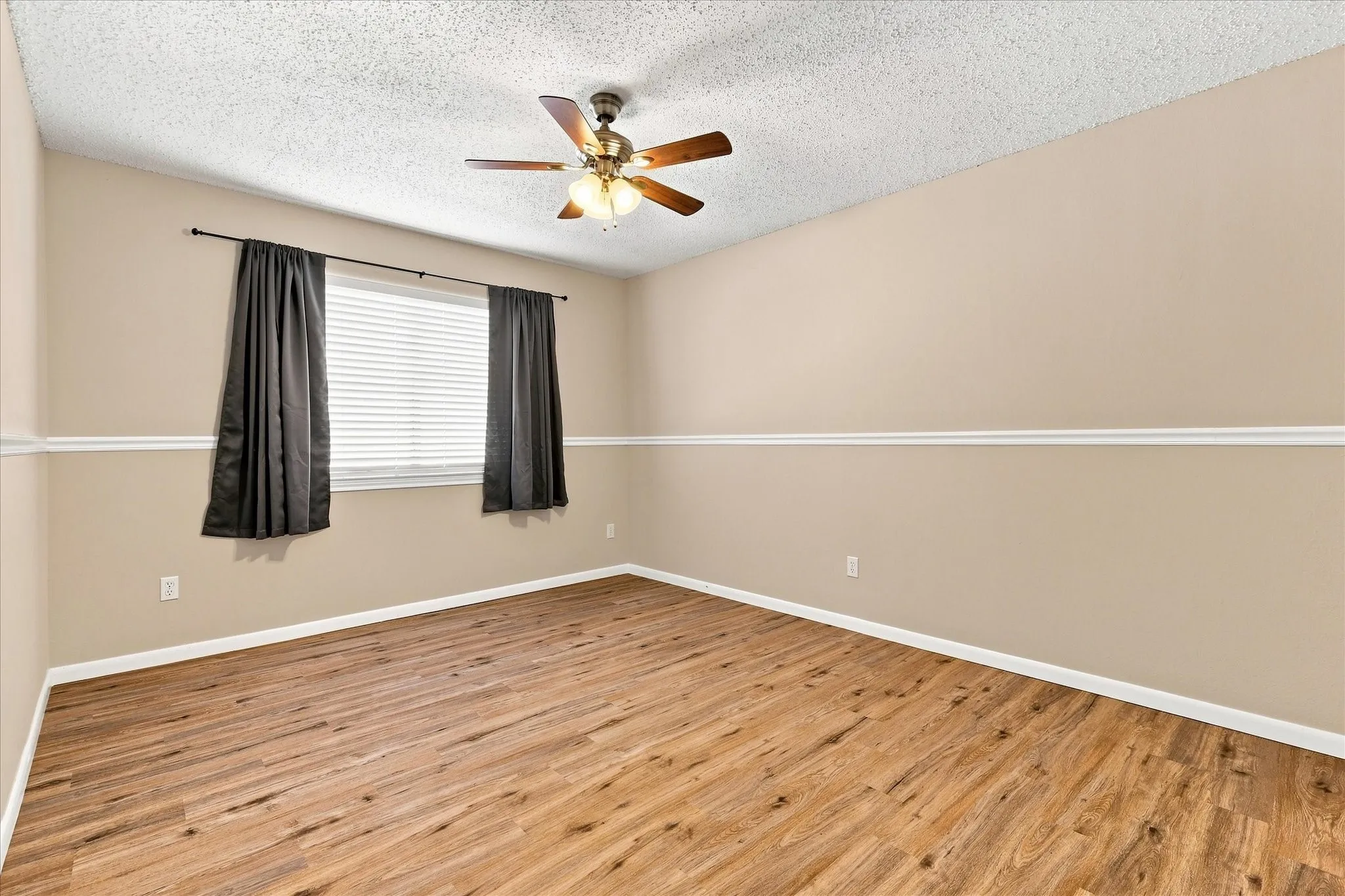 Wood-finish flooring, two-tone painted walls with chair rail molding, ceiling fan with integrated lighting, and window with blinds