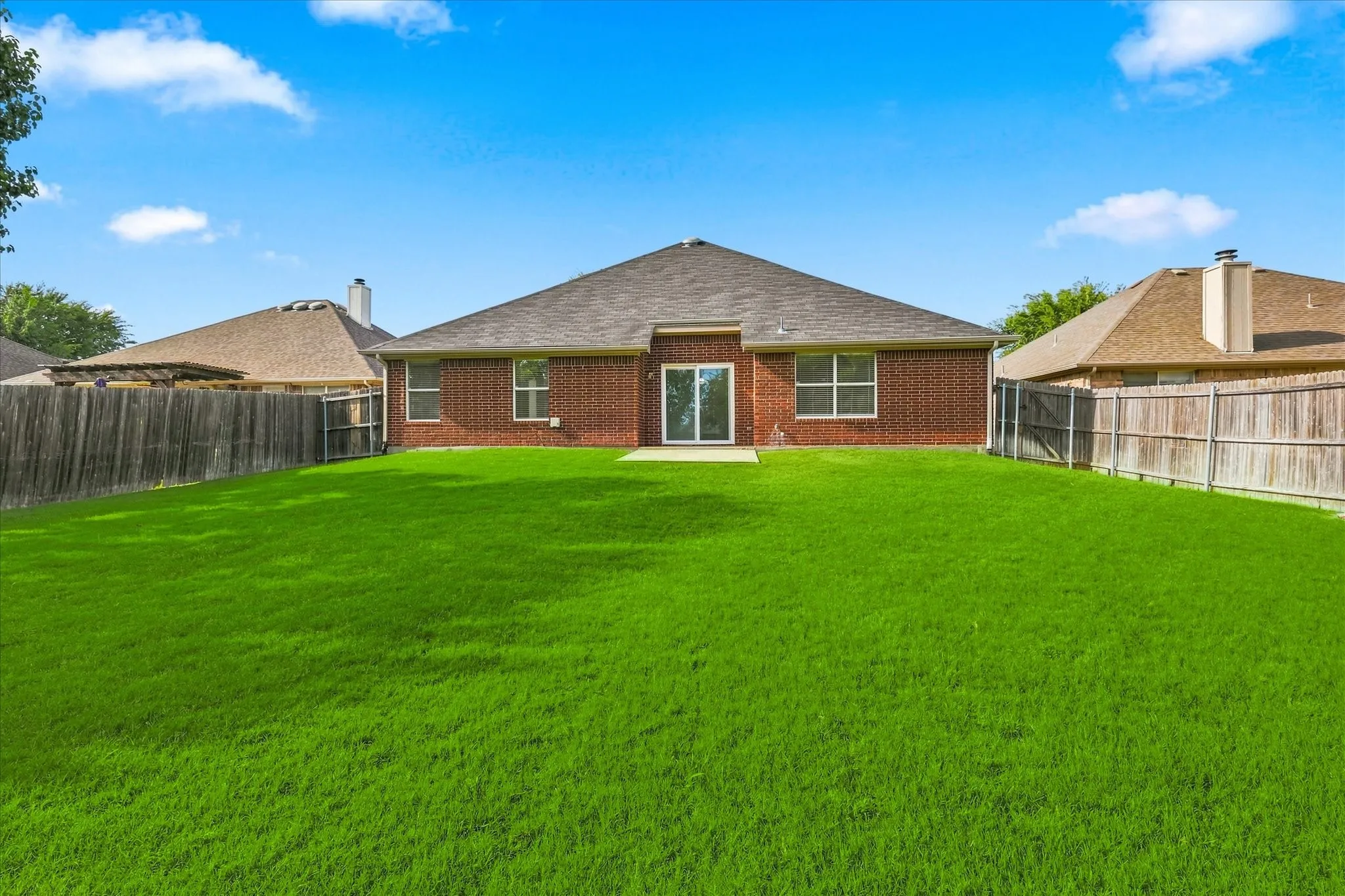 Expansive lawn with a full brick exterior, a concrete patio, and sliding glass doors