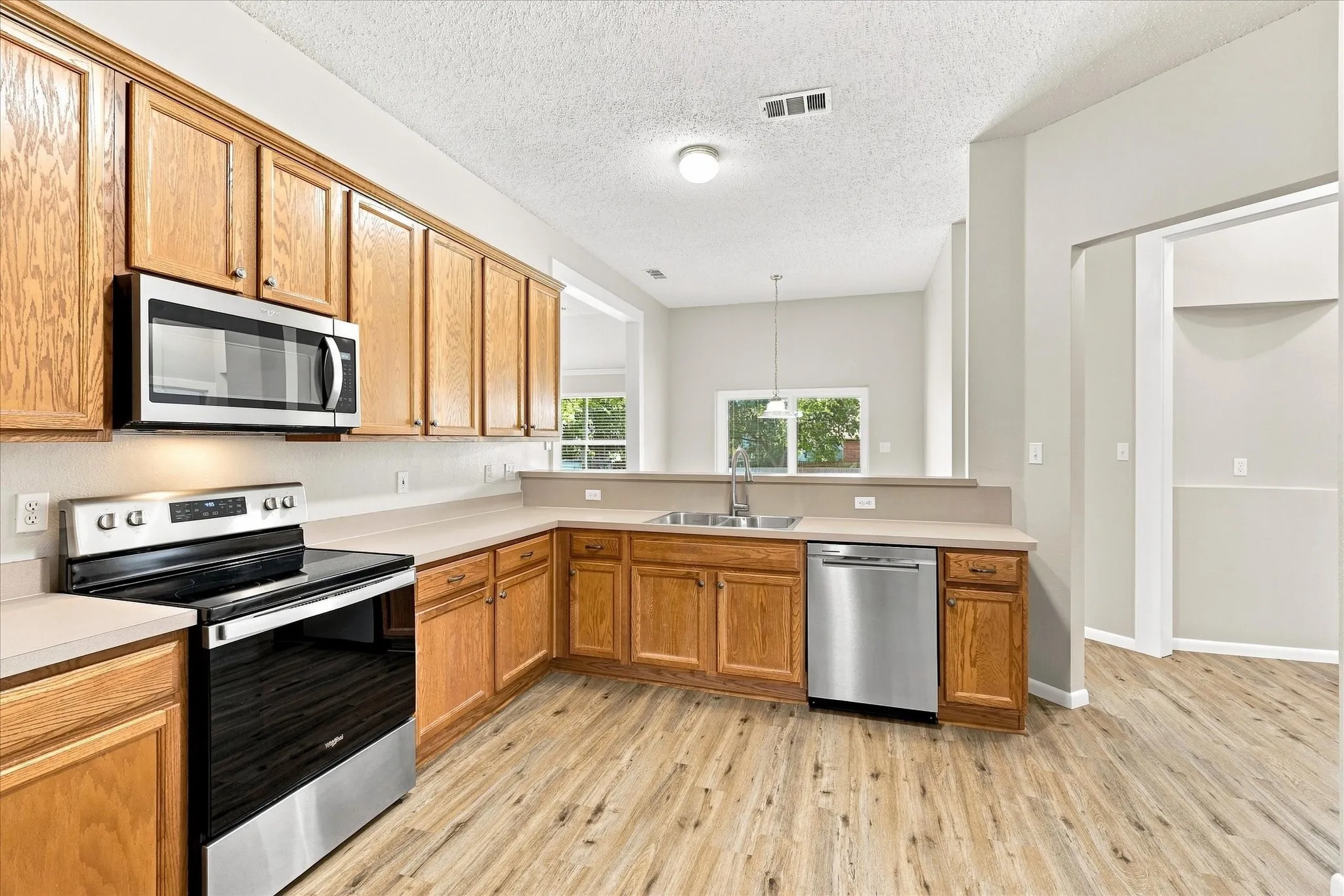 Kitchen featuring wood-finish flooring, stainless steel appliances, light-toned countertops, wood cabinetry, and a stainless steel sink with a gooseneck faucet