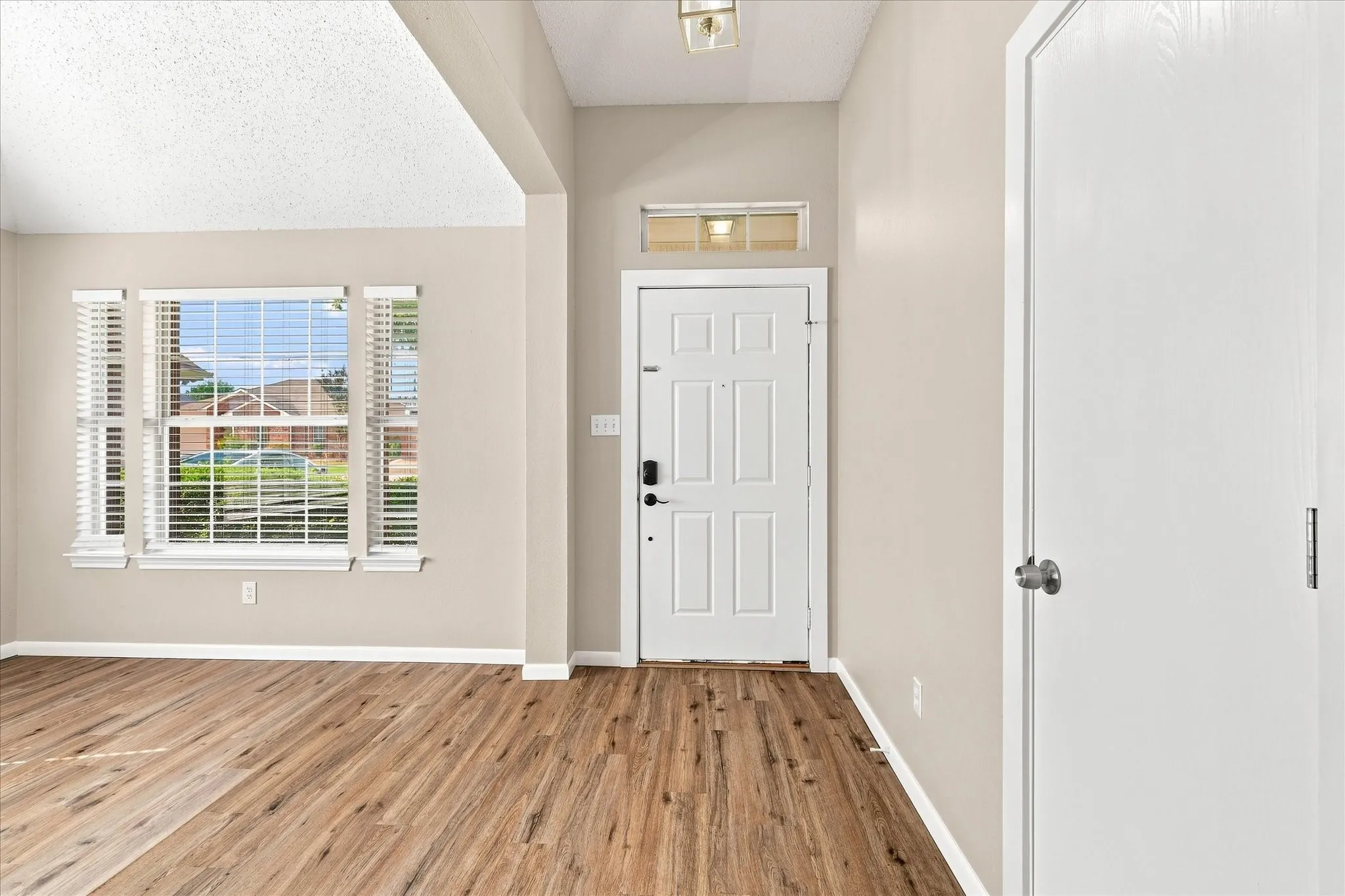 Wood-finish flooring, neutral wall tones, transom window, recessed window with blinds, and a paneled entry door