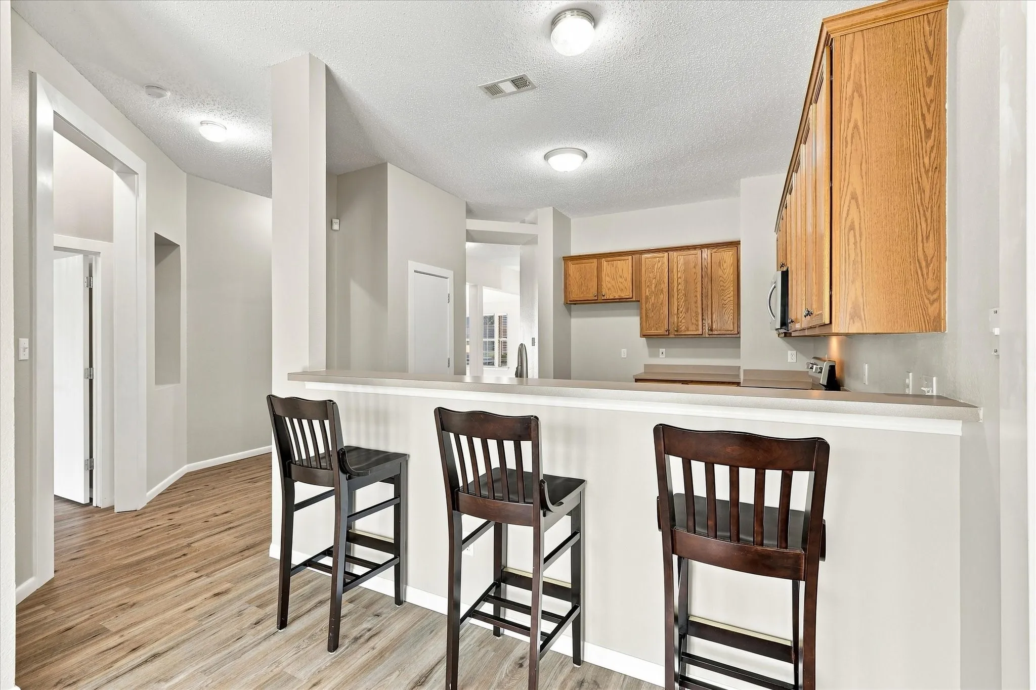Eat-at kitchen peninsula with a light-toned countertop, wood-finish flooring, and natural wood cabinetry