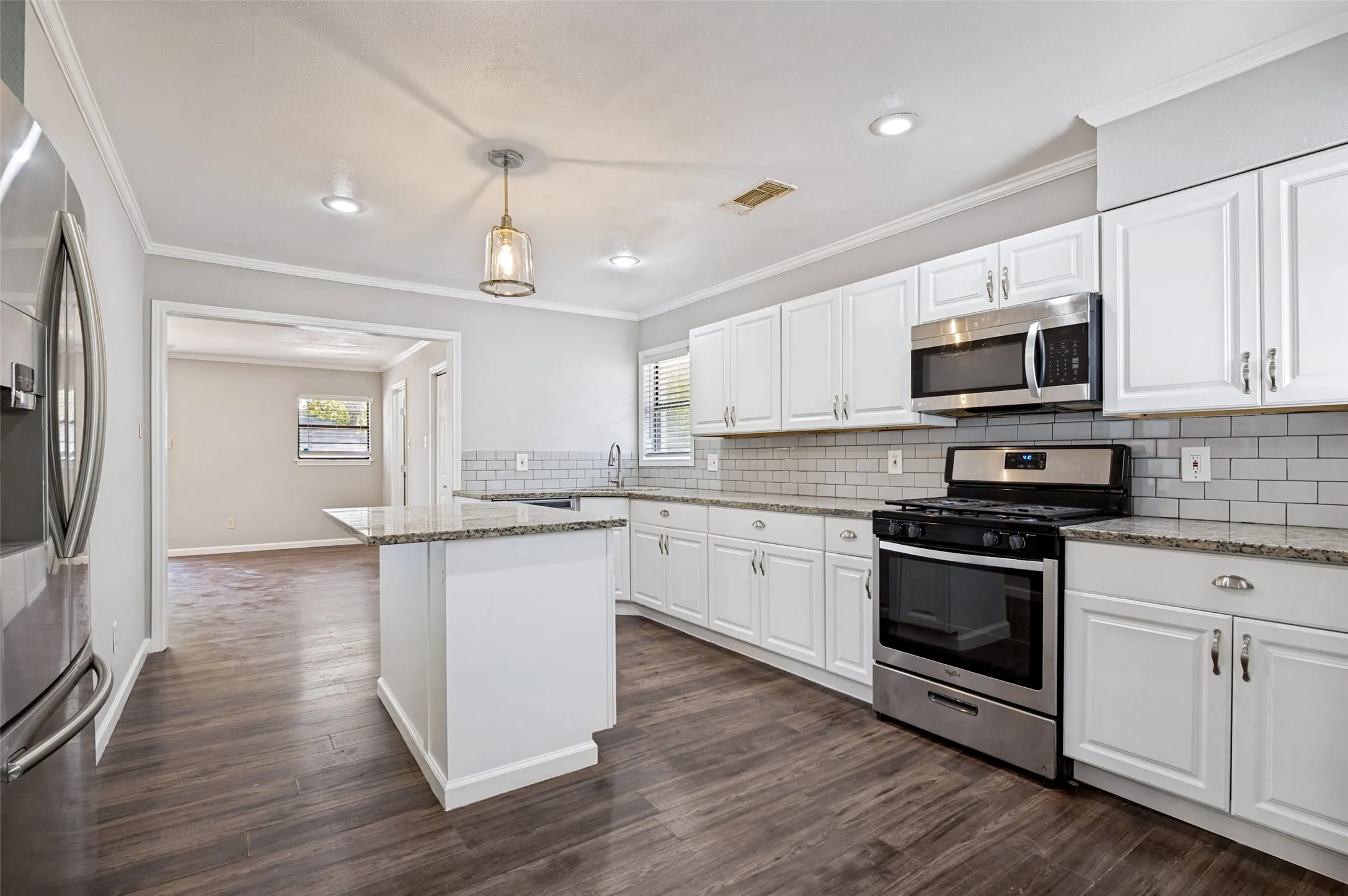 Kitchen featuring white cabinetry, granite countertops, stainless steel appliances, subway tile backsplash, and wood-finish flooring