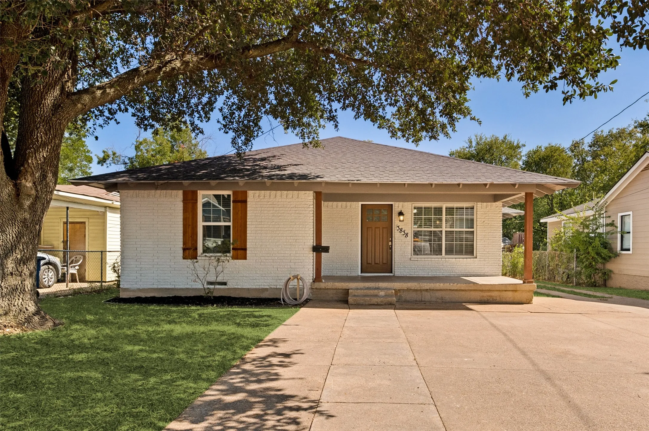 White painted brick exterior with wood shutters, covered porch, and mature tree