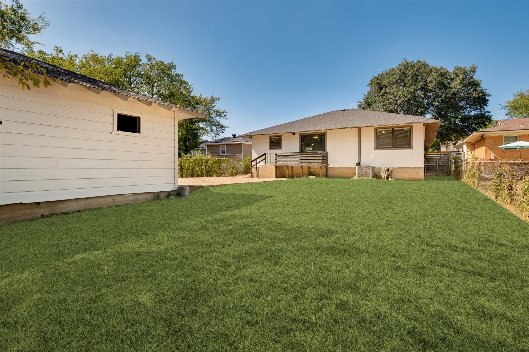 Expansive backyard featuring a large green lawn, an exterior deck, and a detached white siding structure