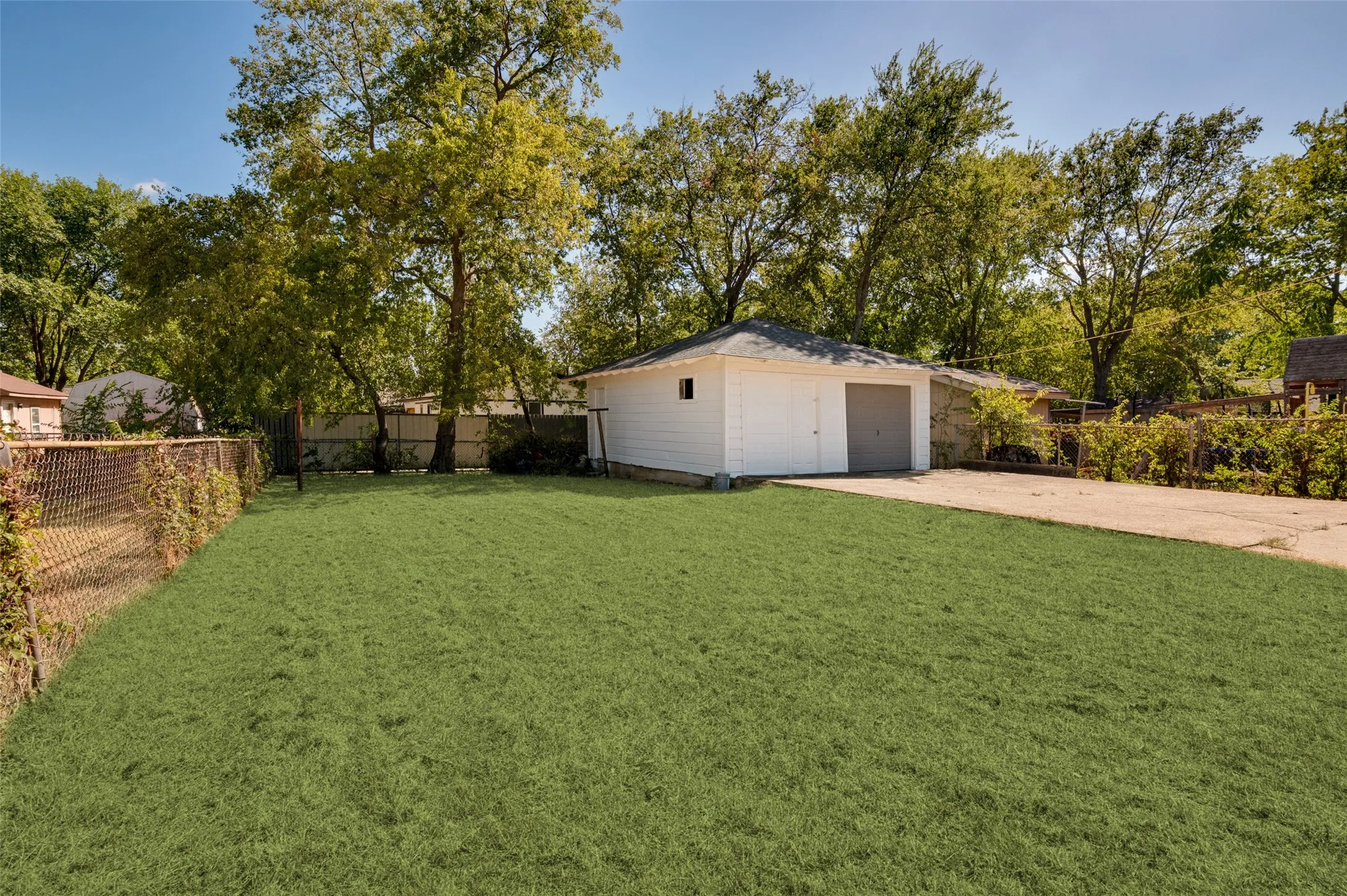 Expansive grassy lawn with a detached garage featuring a gray overhead door and white siding