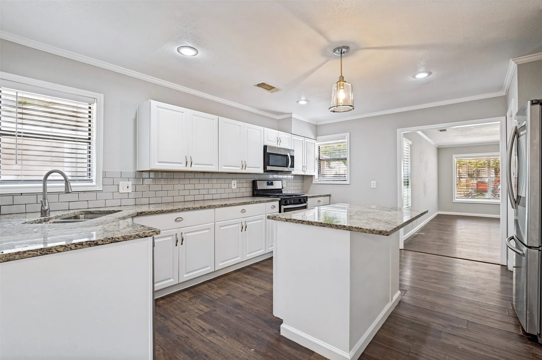 Kitchen featuring white cabinetry, granite countertops, subway tile backsplash, stainless steel appliances, and wood-finish flooring
