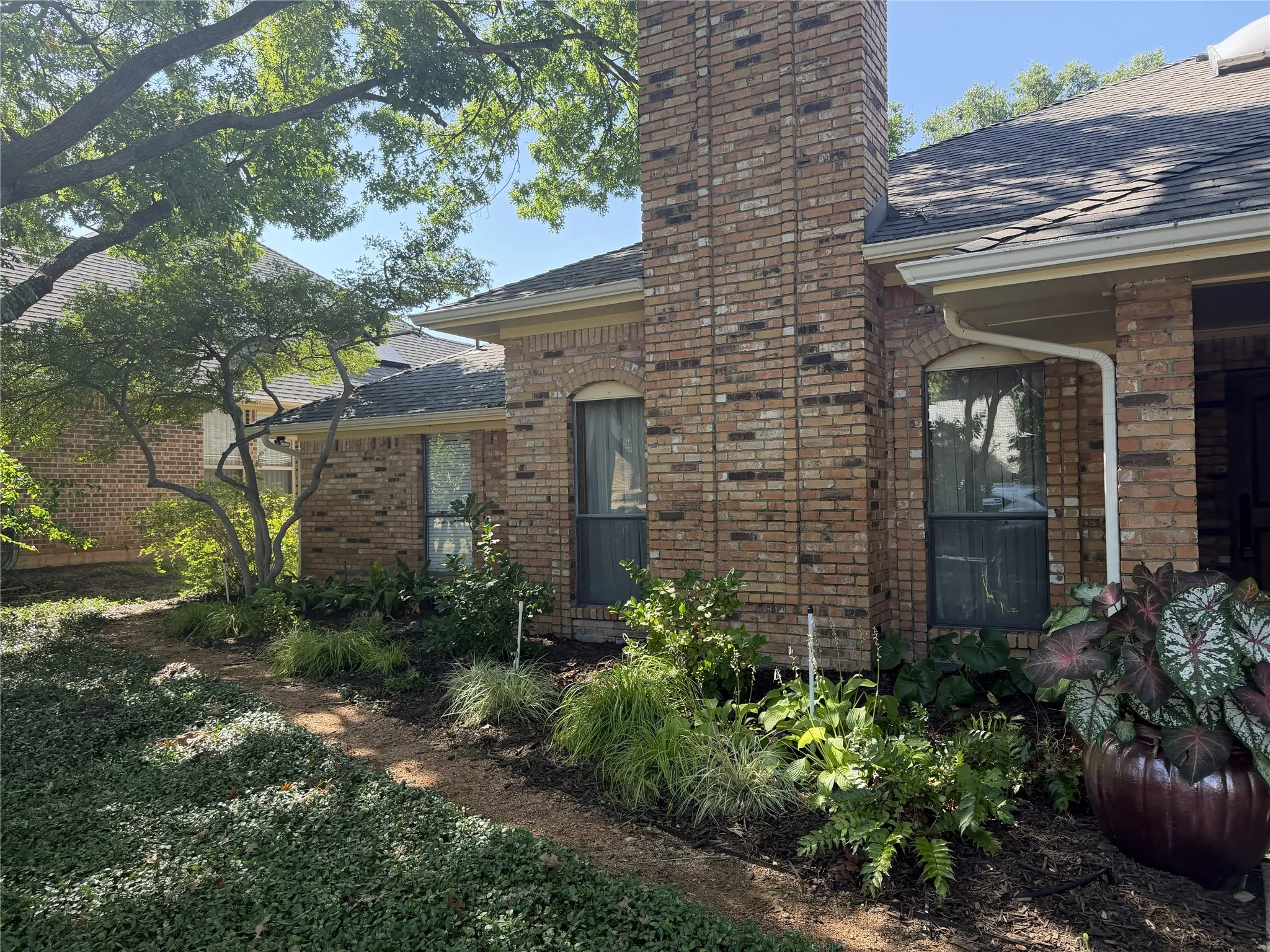Left front of home with gardens are full of shade-loving plantings under the mature tree.