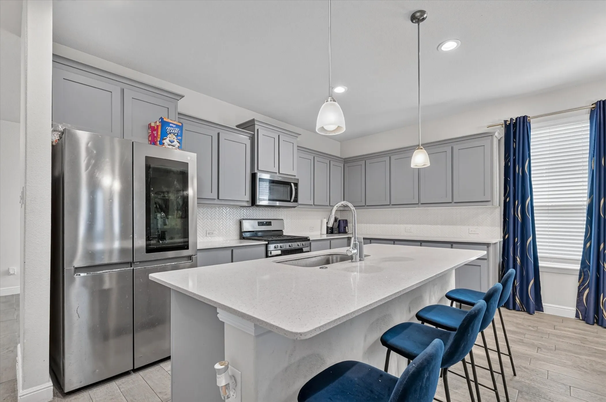 Kitchen featuring grey shaker-style cabinetry, a large kitchen island with a built-in sink, stainless steel appliances, and pendant lighting