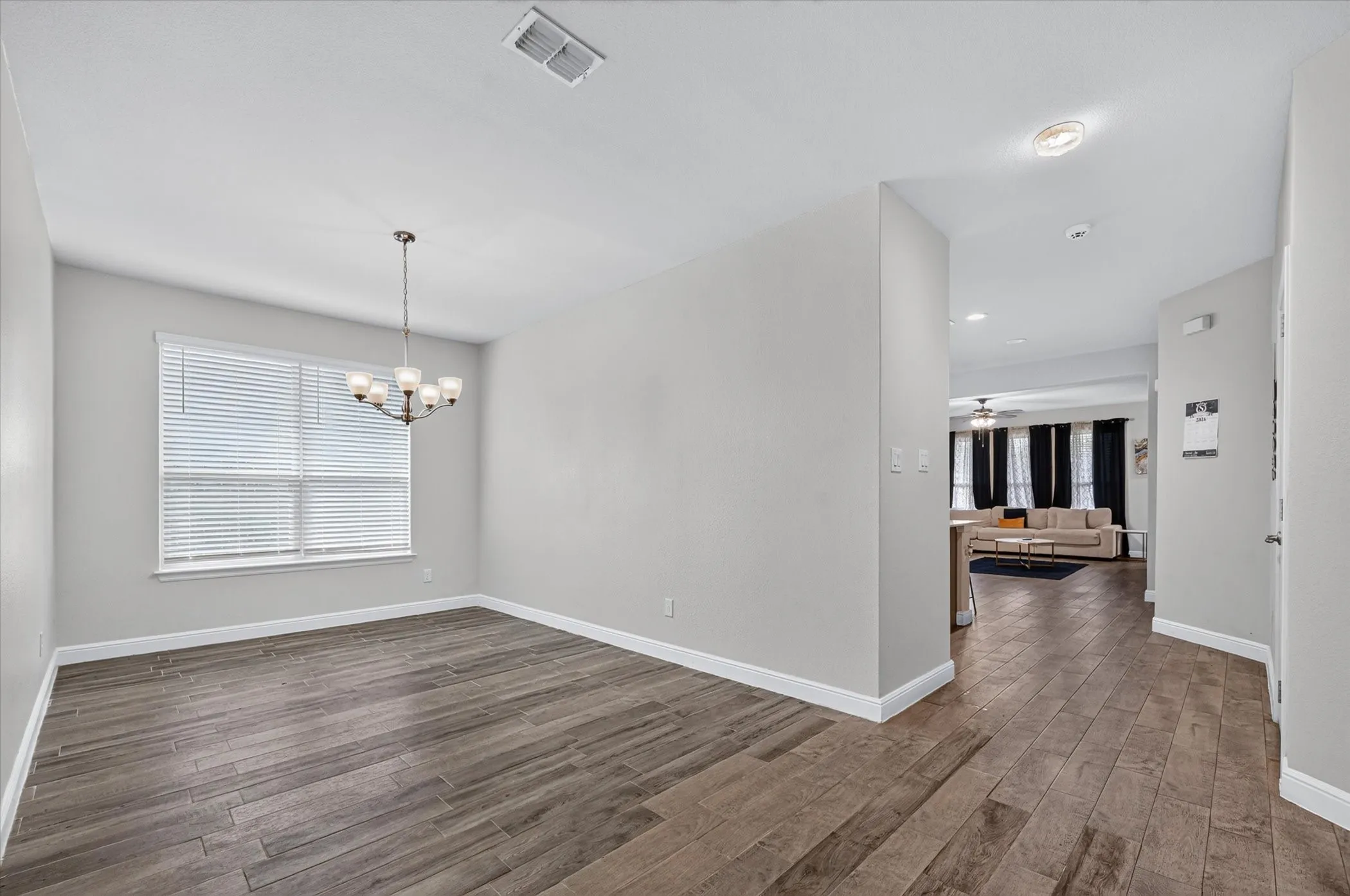 Spacious room with wood-finish flooring, a contemporary chandelier, and ample natural light from the large window