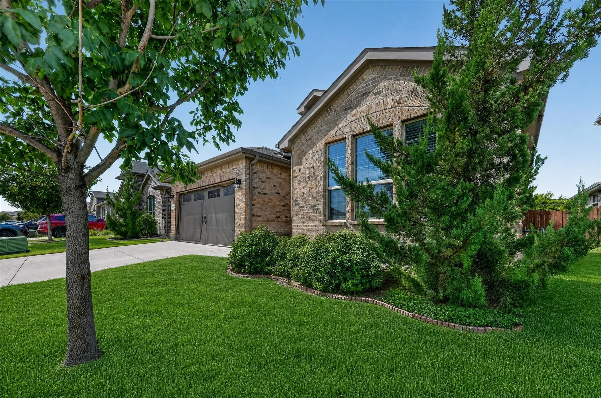 Brick exterior, arched window, attached garage, concrete driveway, and established landscaping
