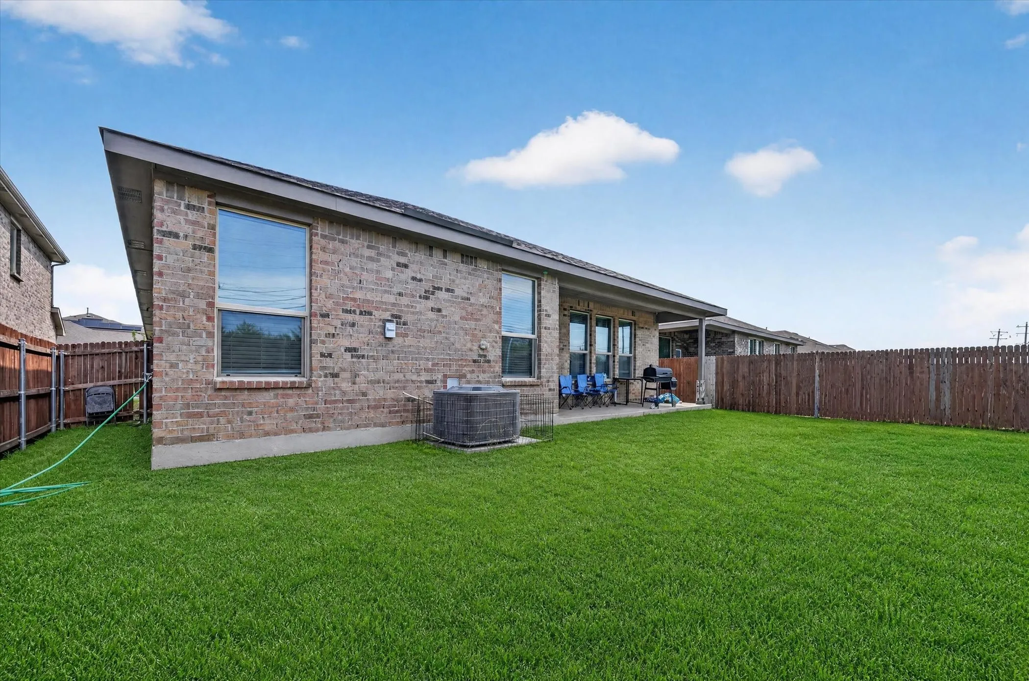 Expansive backyard with a manicured lawn, brick exterior, covered patio, and privacy fencing