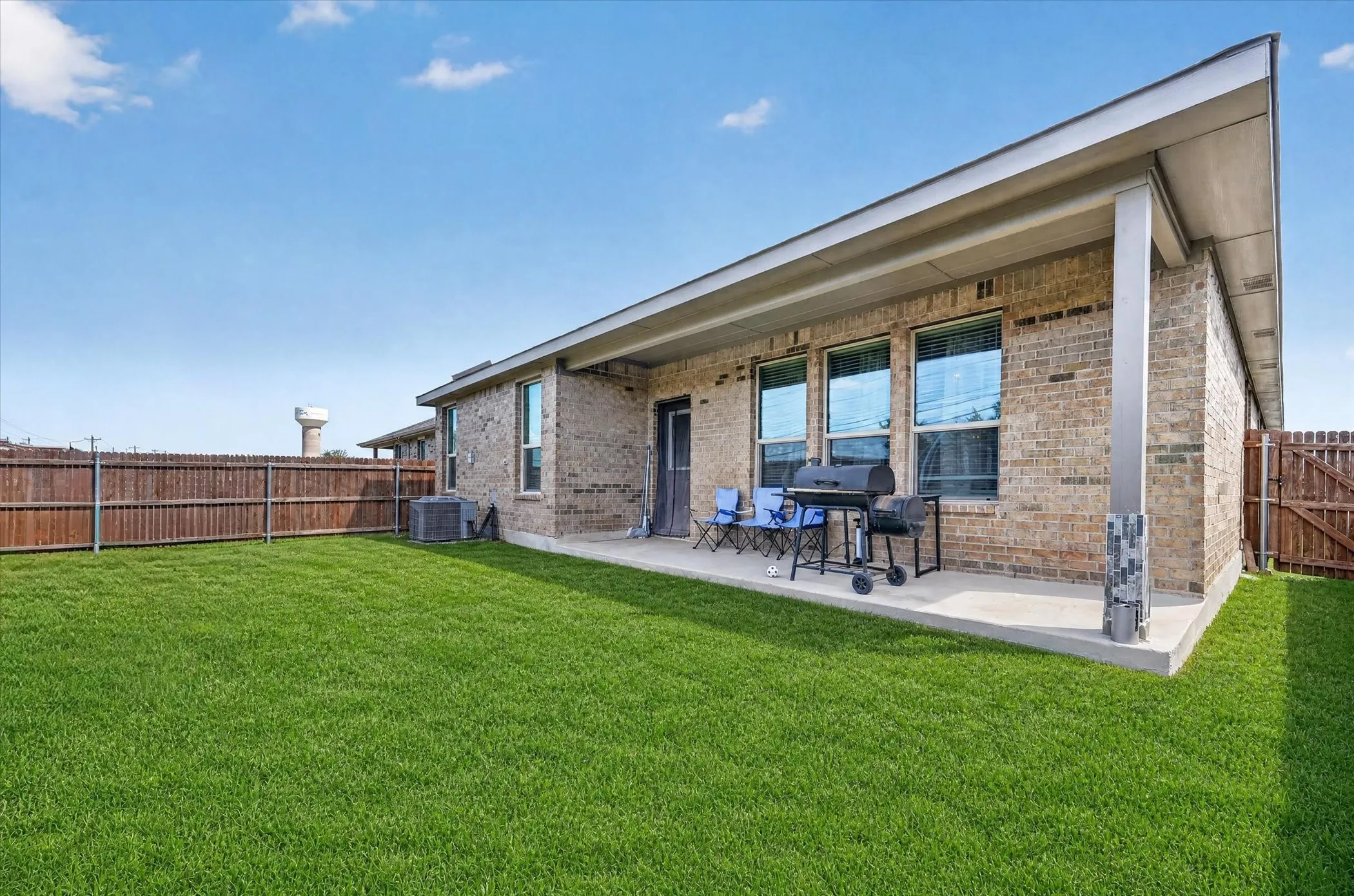 Expansive green lawn, wood fence, concrete patio, brick exterior, and covered outdoor area