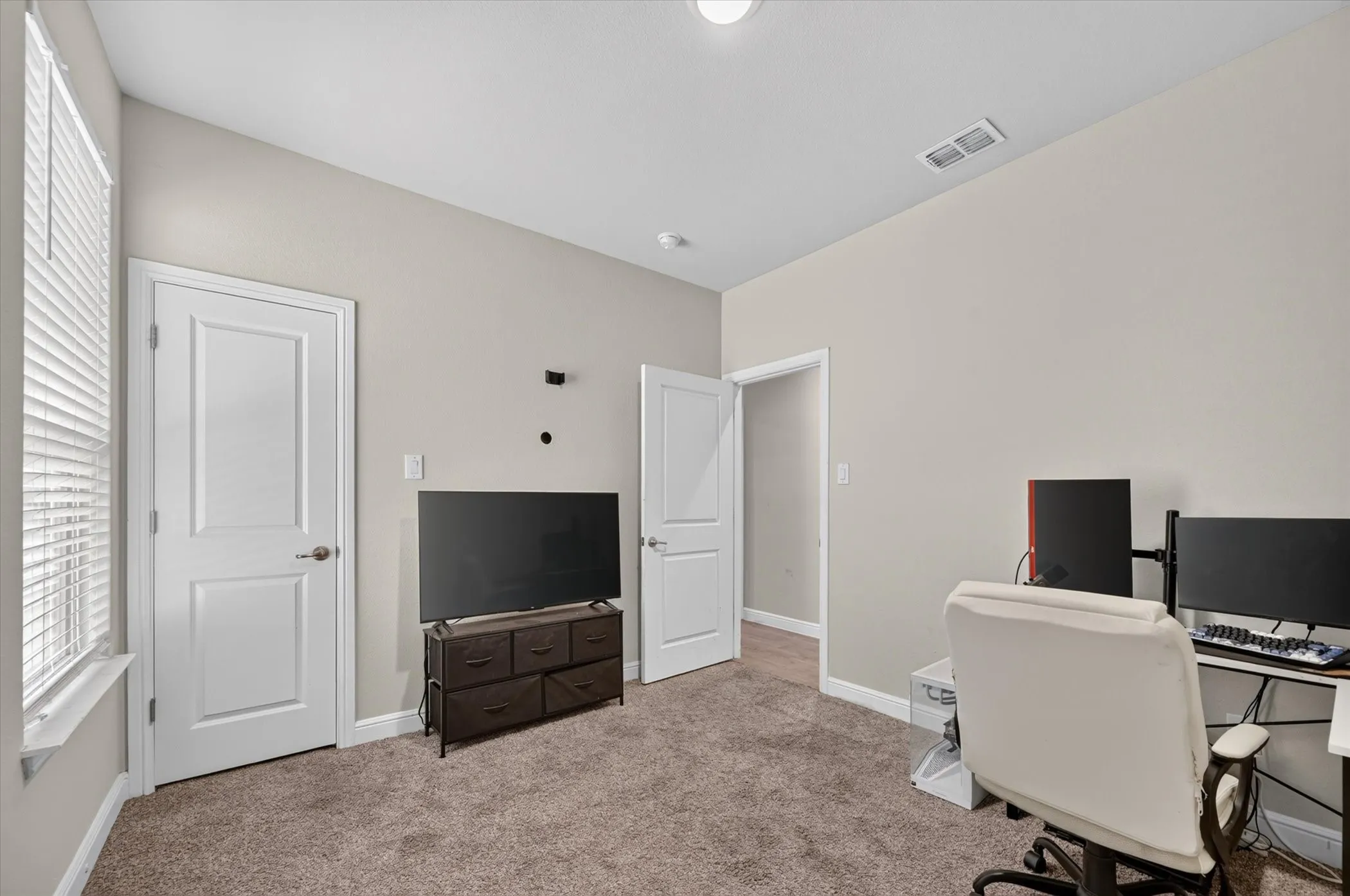 Carpeted room with a vaulted ceiling, multiple white panel doors, and a window featuring horizontal blinds