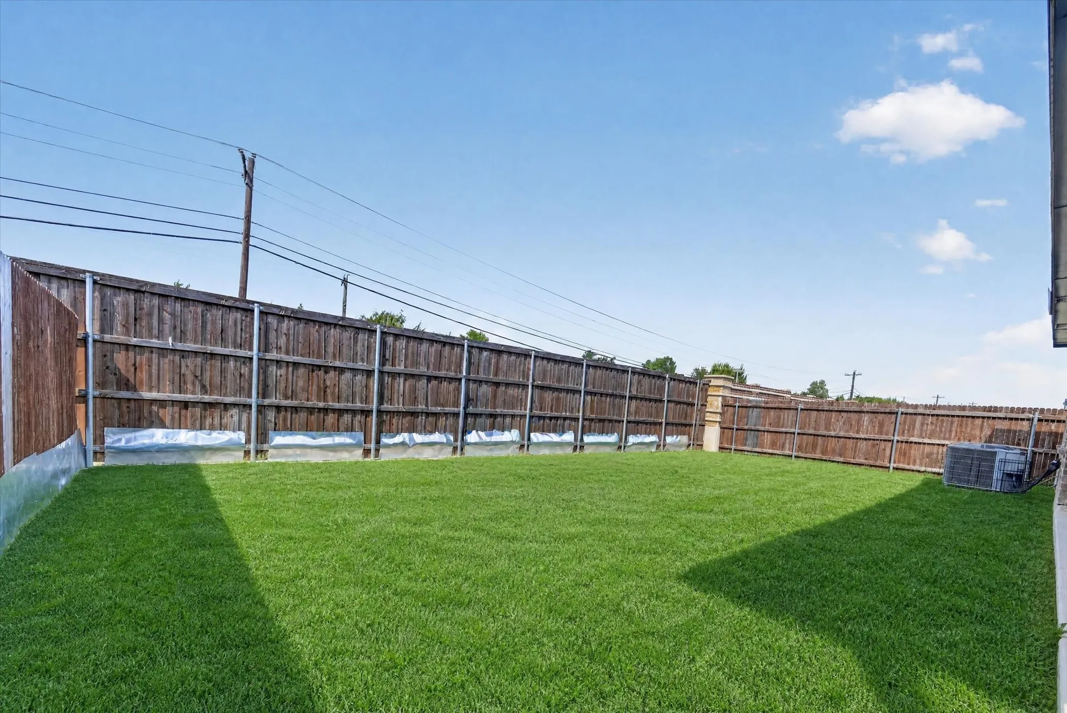 Expansive grassy yard area featuring full wood panel fencing and an air conditioning unit