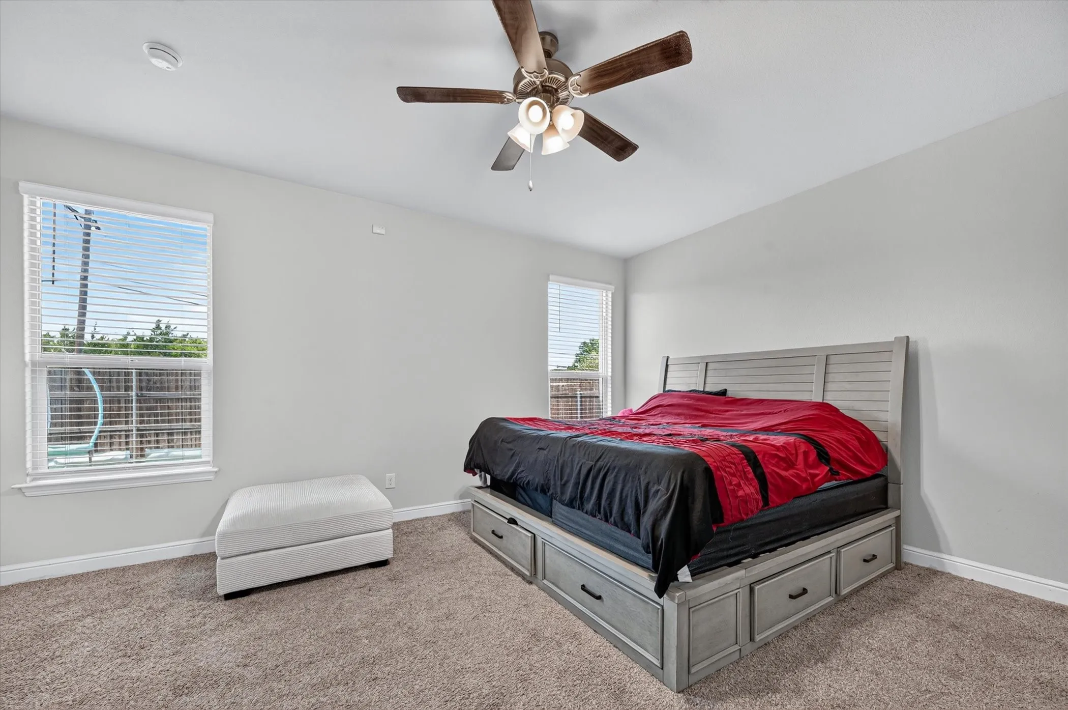 Ceiling fan with integrated lighting, two large windows, light gray walls, and carpeted flooring