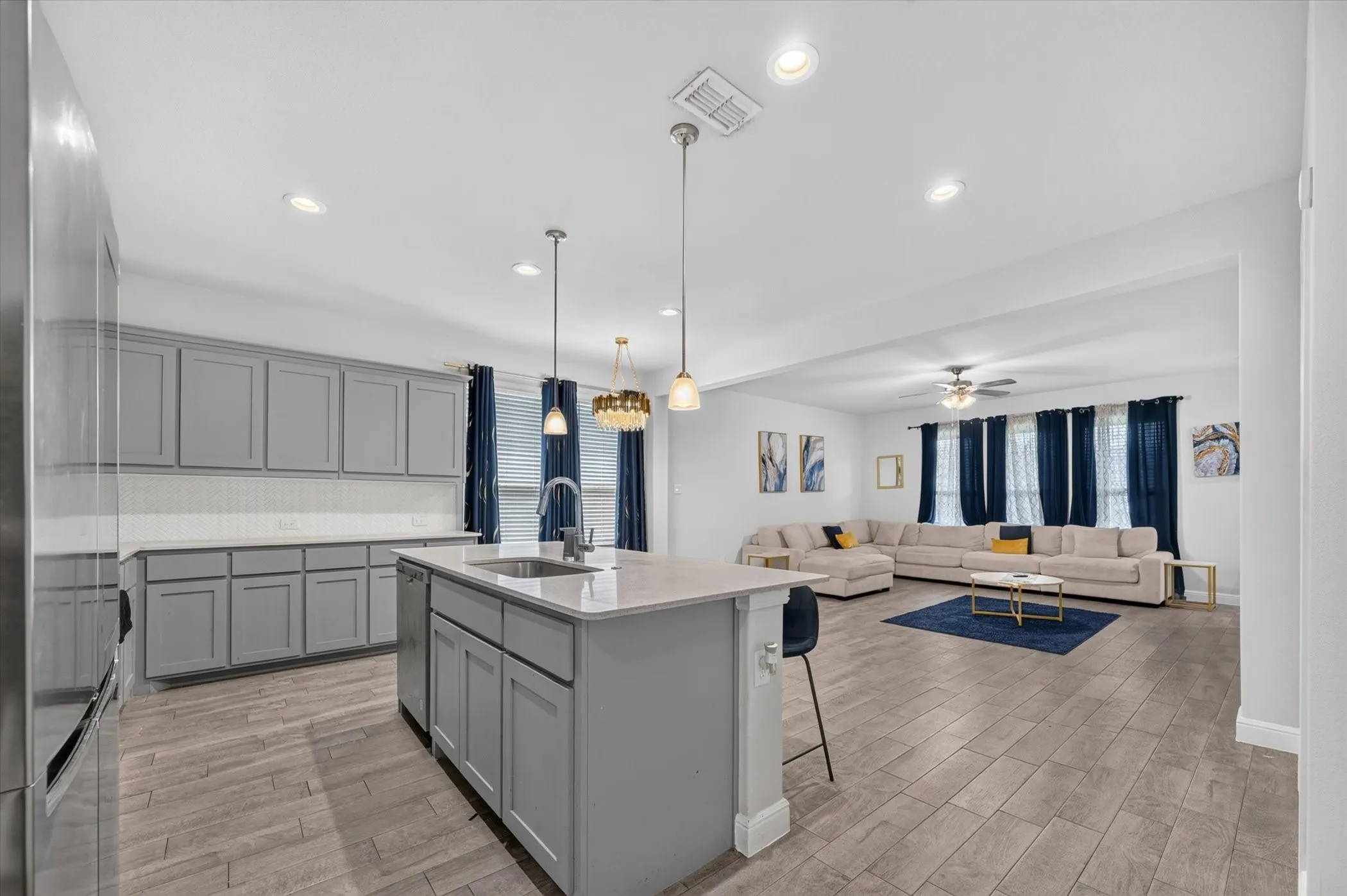 Kitchen featuring an island with a built-in sink, gray cabinetry, light-colored countertops, and a white tile backsplash