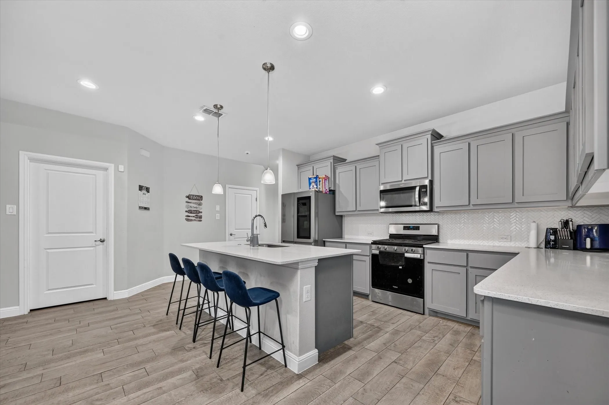 Kitchen featuring wood-finish flooring, an island with pendant lighting, gray cabinetry, stainless steel appliances, and a chevron tile backsplash