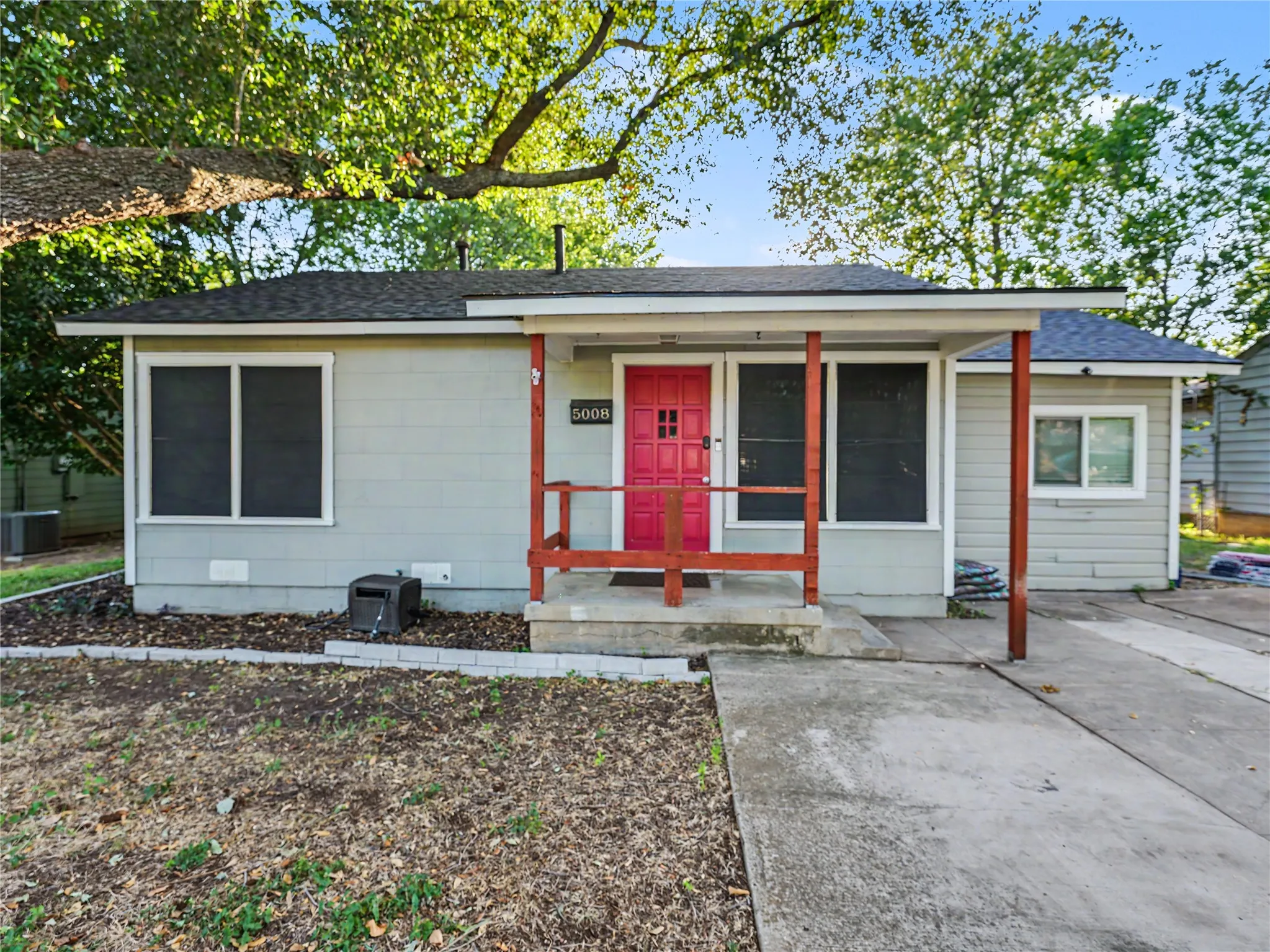 Single-story property with light gray siding, a covered front porch with red railing, a vibrant red front door, and a concrete driveway
