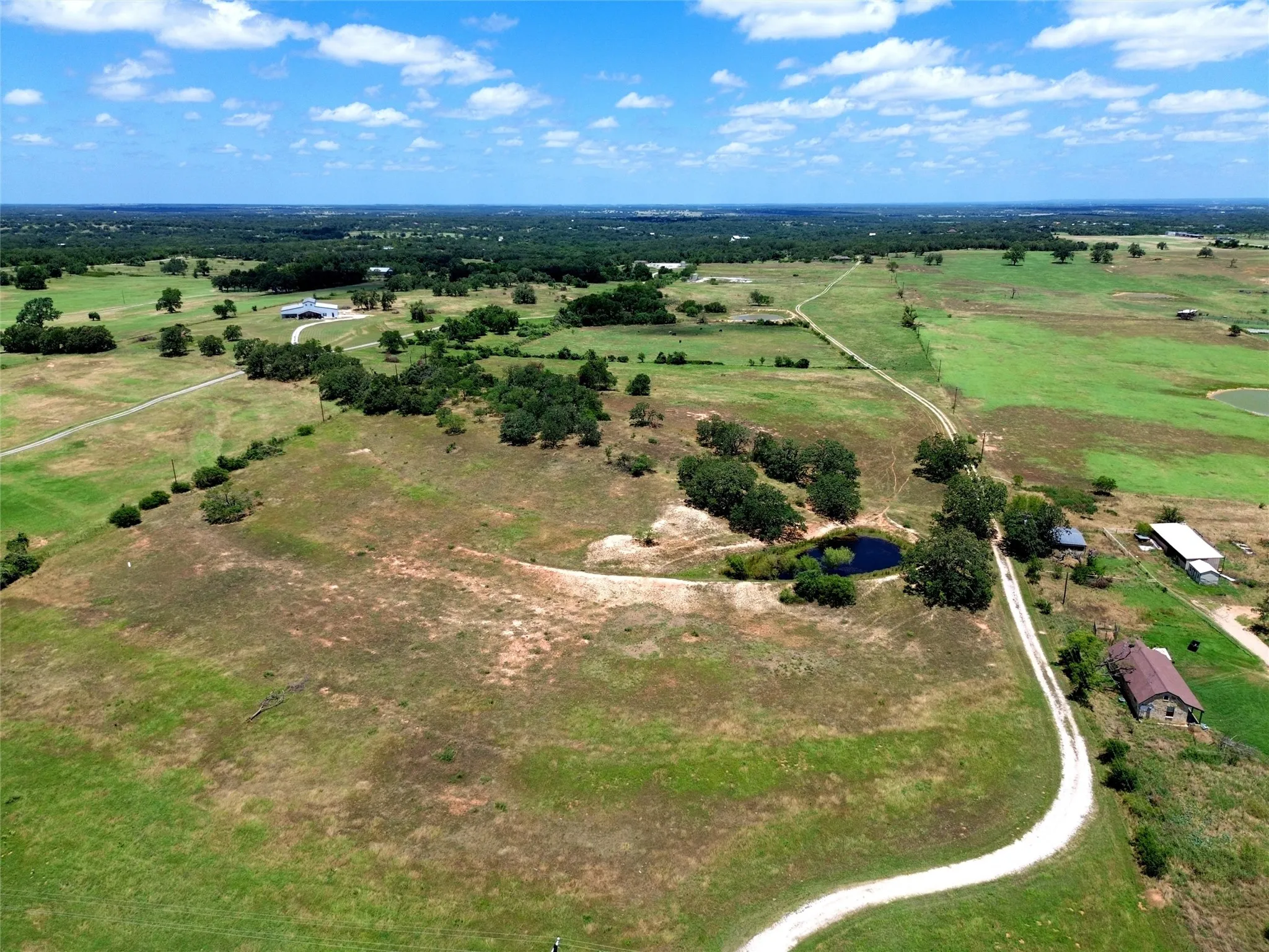 Expansive acreage with scattered trees, a natural pond, and multiple structures