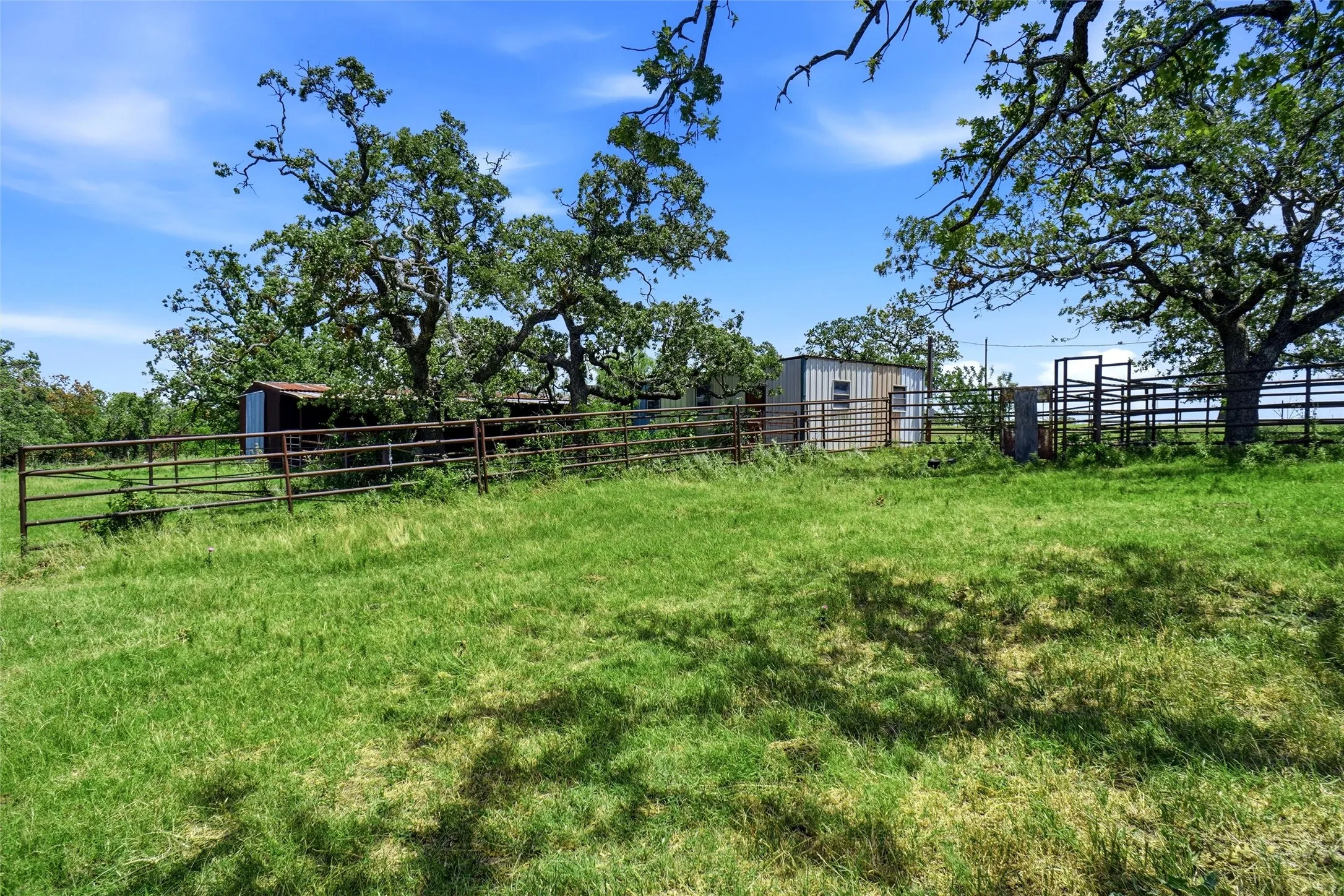 Extensive grassy terrain with mature trees, perimeter fencing, and a metal utility structure
