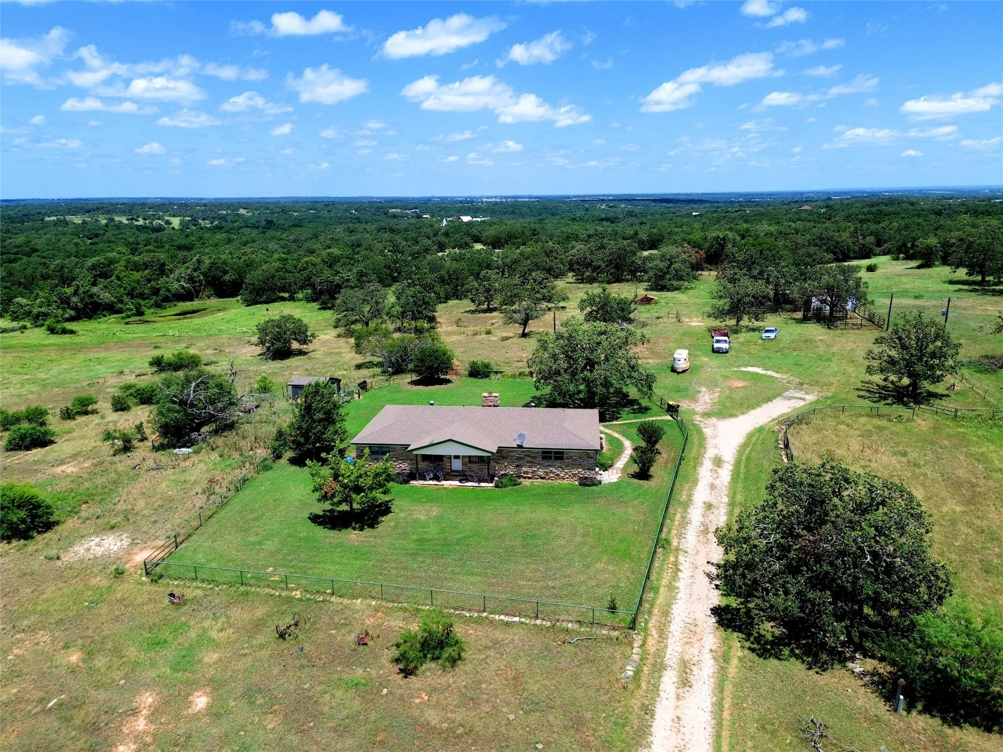 Stone exterior residence with a fenced perimeter, expansive manicured lawn, and a gravel driveway
