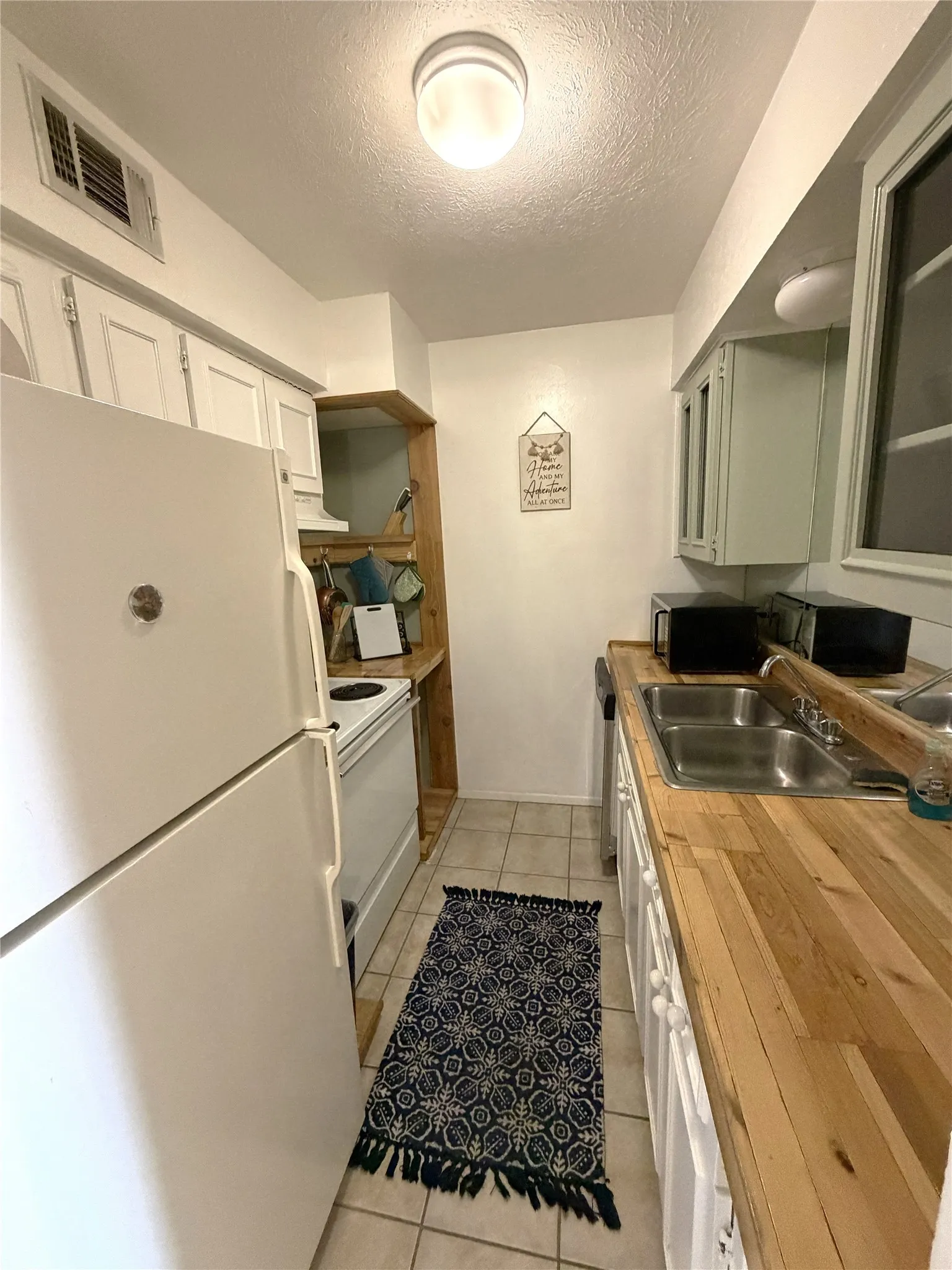 White cabinetry, light wood-finish countertops, tile flooring, and a stainless steel double basin sink