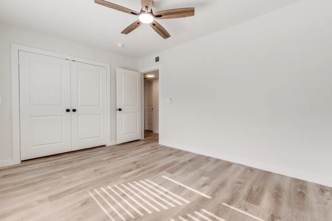 Wood-finish flooring, white walls, white paneled bifold closet doors, and a ceiling fan with light