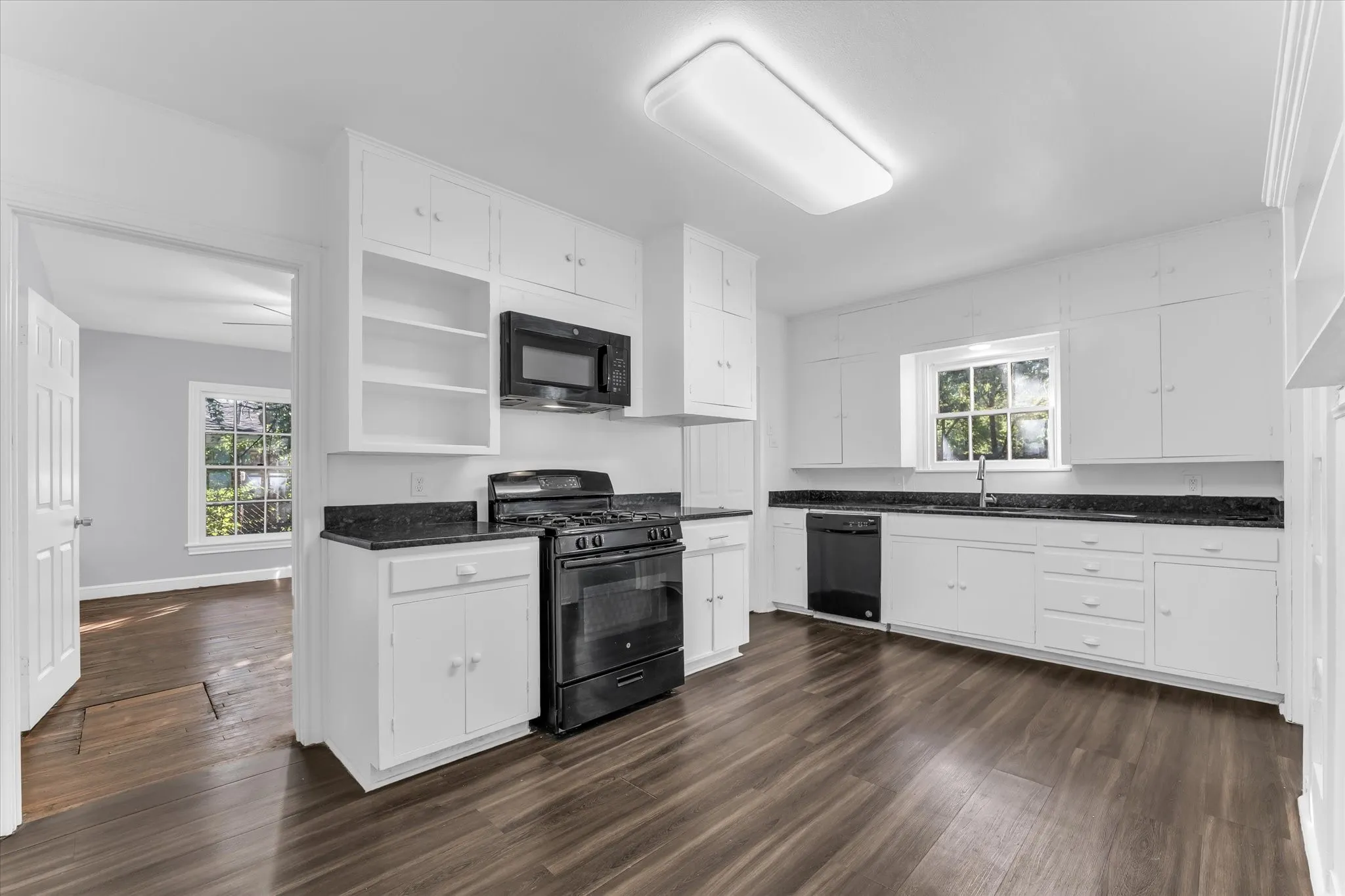 Kitchen featuring wood-finish flooring, white cabinetry, dark countertops, and a black appliance suite including a range, microwave, and dishwasher