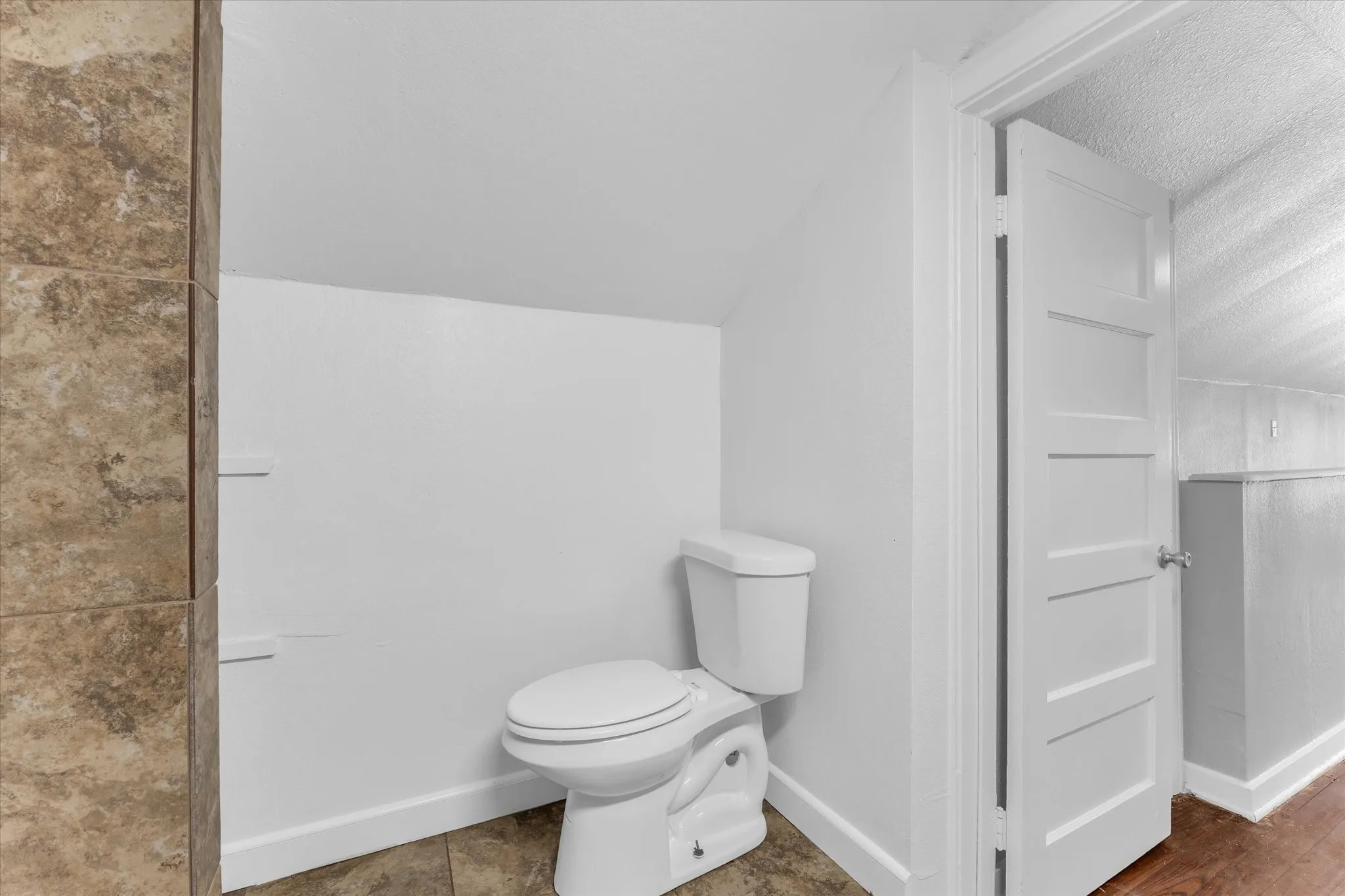 Sloped ceiling, tiled flooring, built-in shelving, paneled interior door, white toilet