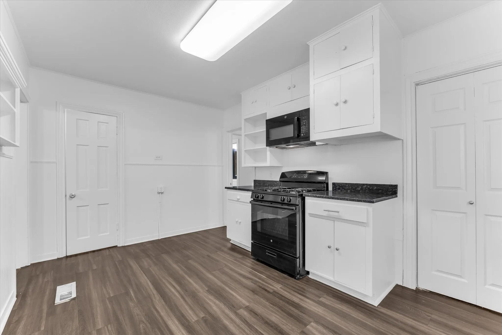 Wood-finish flooring, white cabinetry, black countertops, built-in microwave, and a gas range