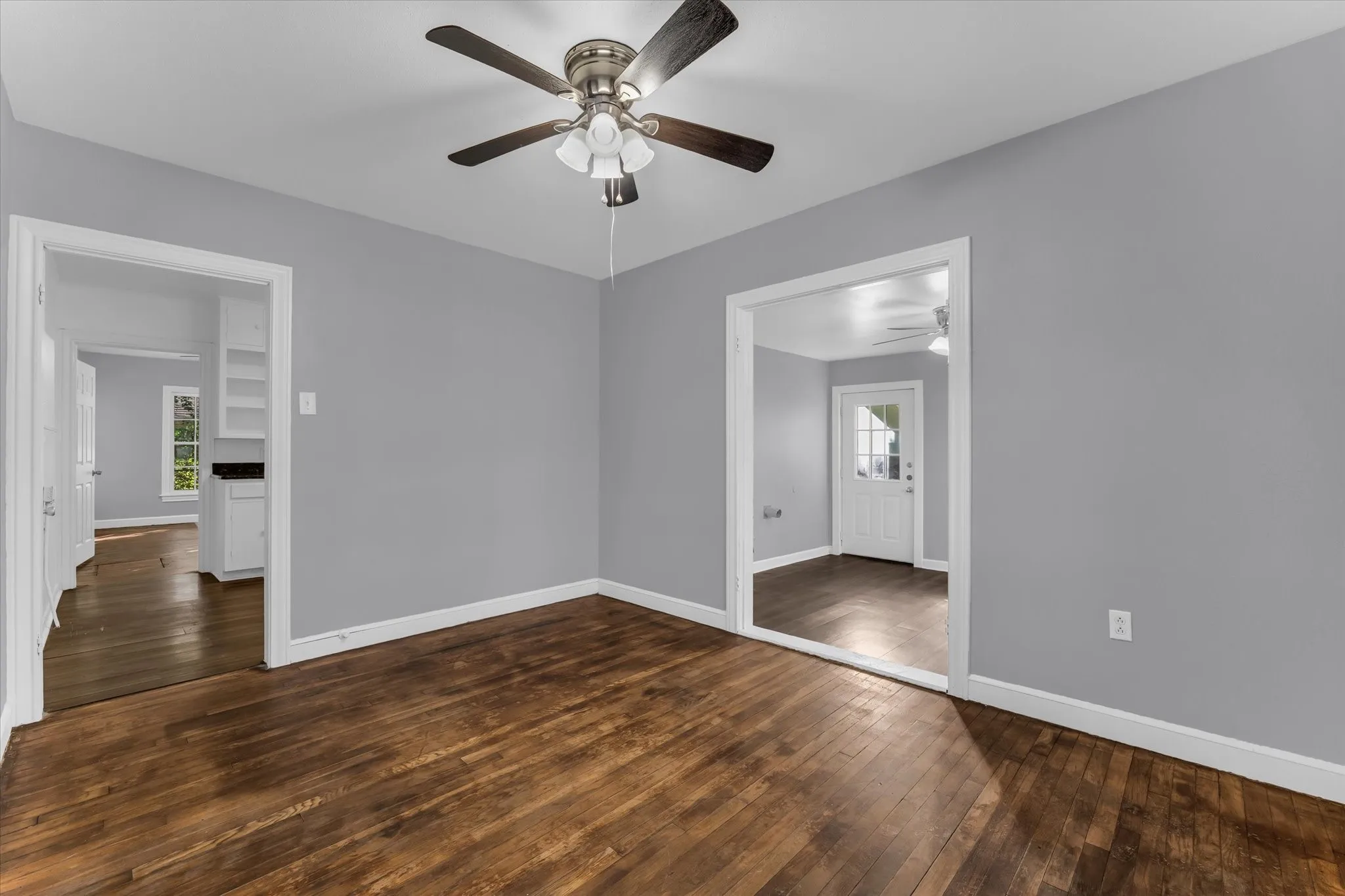 Hardwood flooring complemented by light gray walls, white trim, and a ceiling fan with integrated lighting