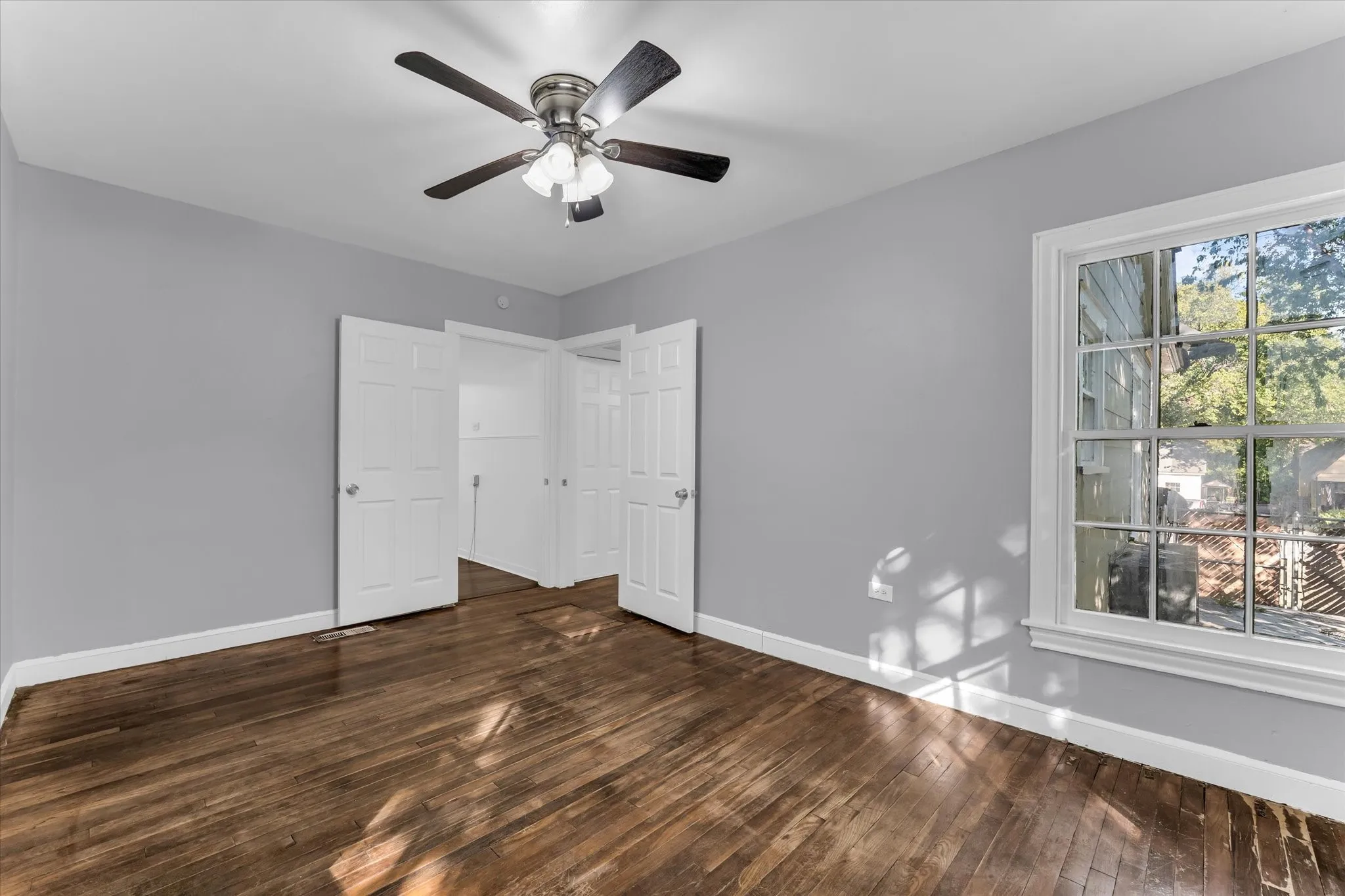 Hardwood flooring, painted walls, ceiling fan, white trim, and a multi-pane window