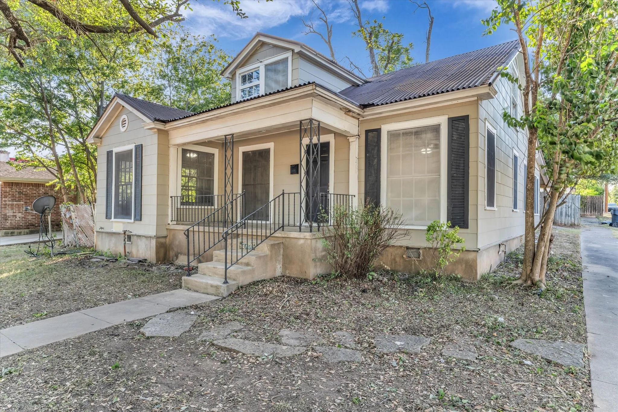 Exterior featuring a corrugated metal roof, dormer window, covered porch, and concrete steps with wrought iron railings