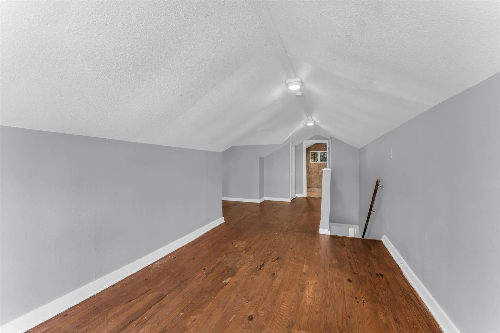 Vaulted ceiling with recessed lighting, wood-finish flooring, light gray wall paint, and white trim