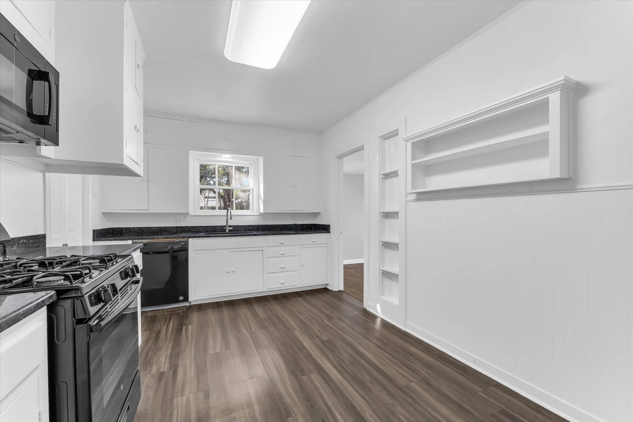 Kitchen featuring wood-finish flooring, white cabinetry, dark countertops, and black appliances