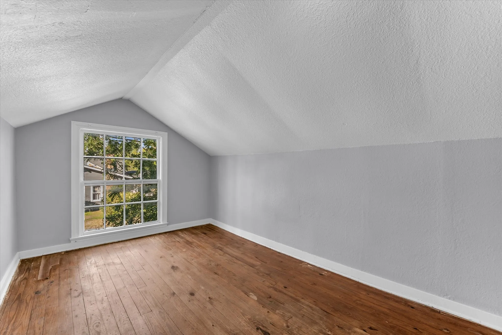 Attic room with wood-finish flooring, white trim, and a multi-pane window