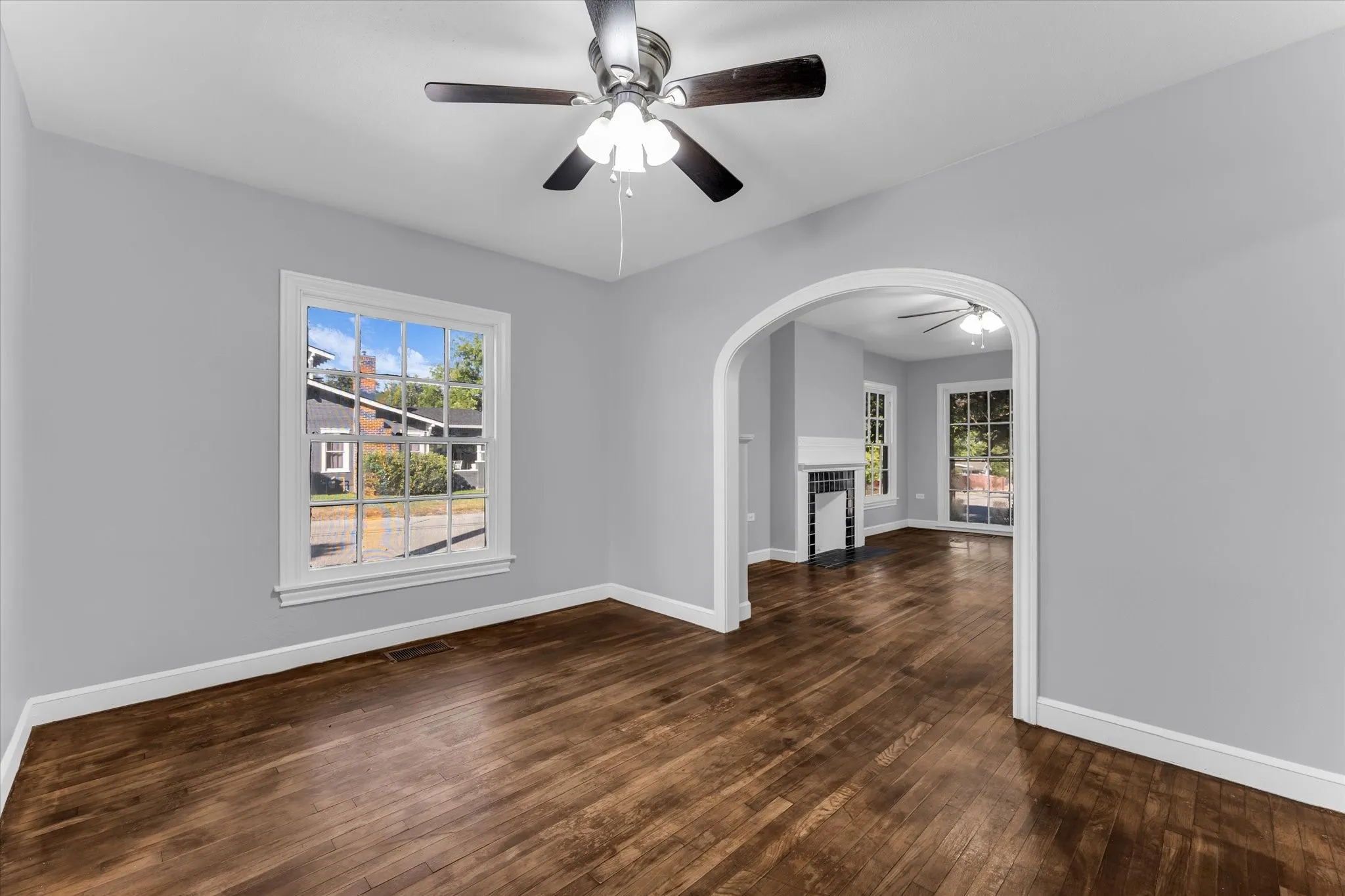 Hardwood flooring throughout, neutral wall tones, arched doorway, and ceiling fans with integrated lighting