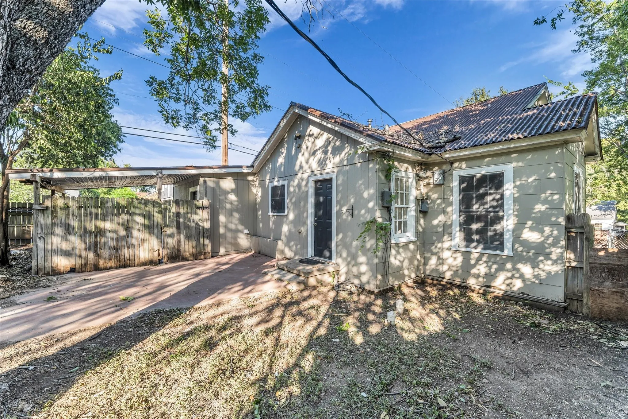 Corrugated metal roofing, light-toned exterior siding, and a covered carport with wood fencing