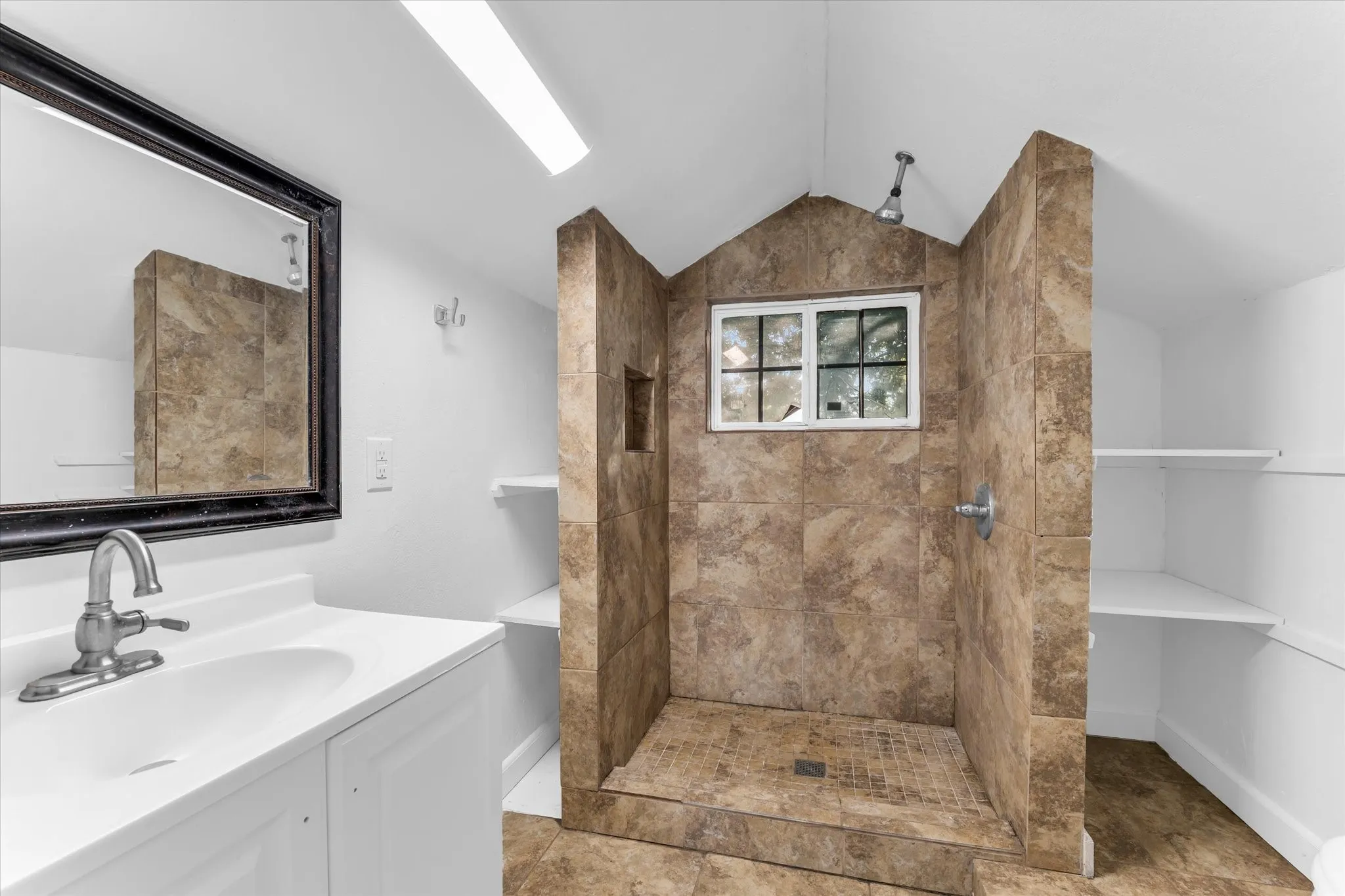 Walk-in shower with tiled walls and flooring, white vanity with integrated sink, framed mirror, and built-in shelving