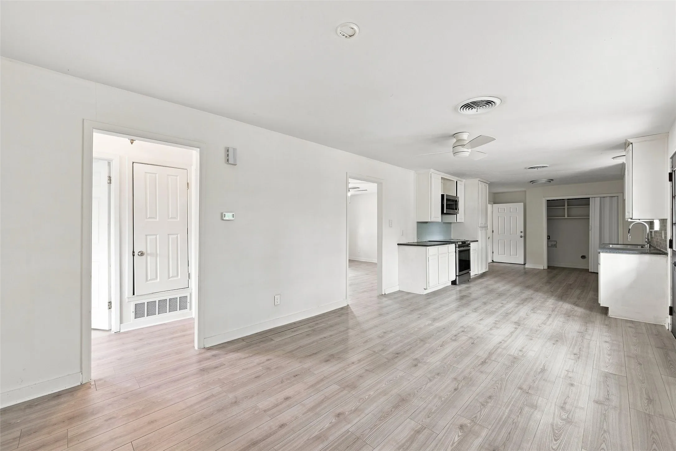 Open-concept living space with wood-finish flooring, white cabinetry, dark countertops, and a ceiling fan