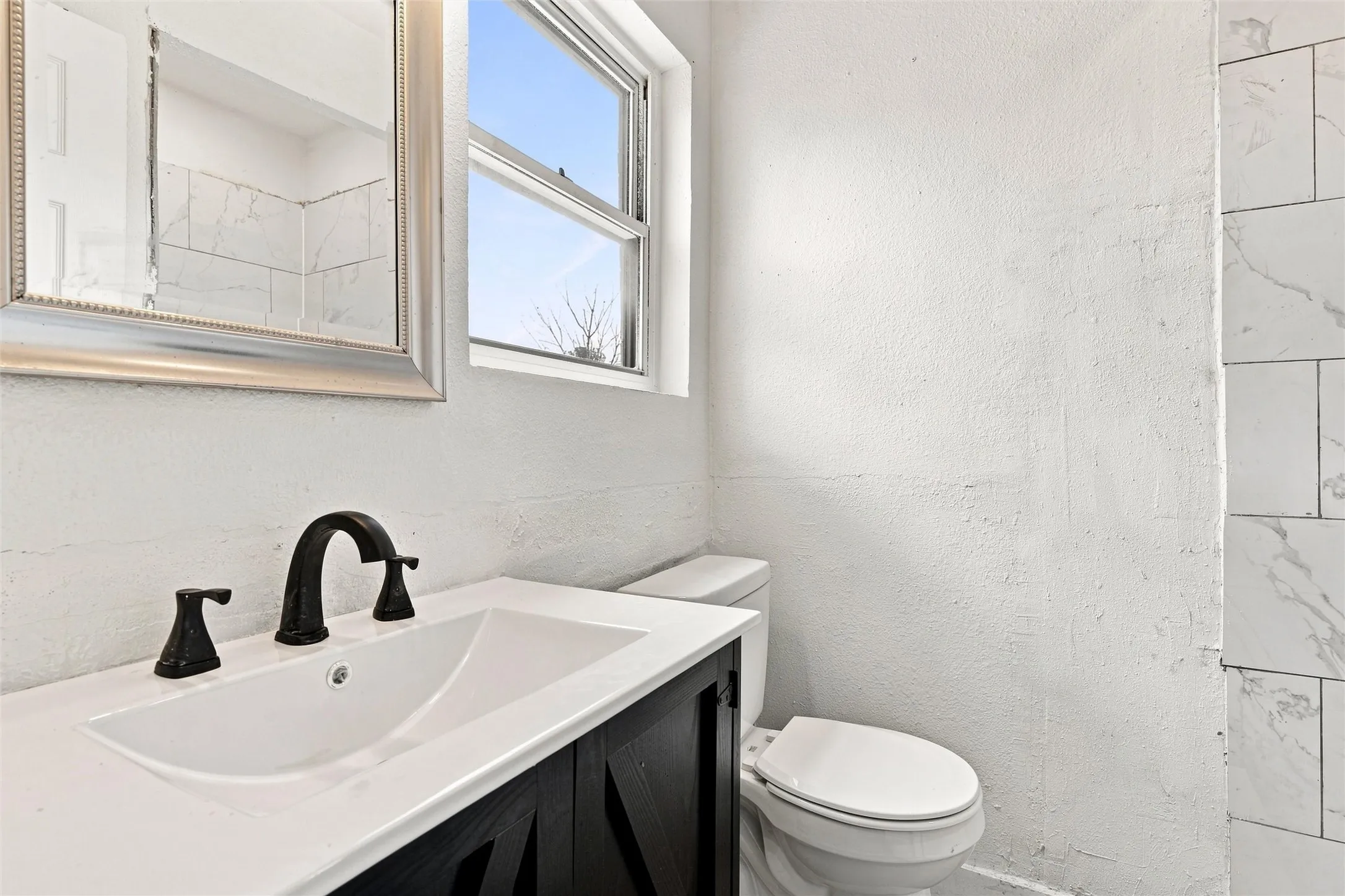 White vanity with integrated sink, black hardware, framed mirror, and window