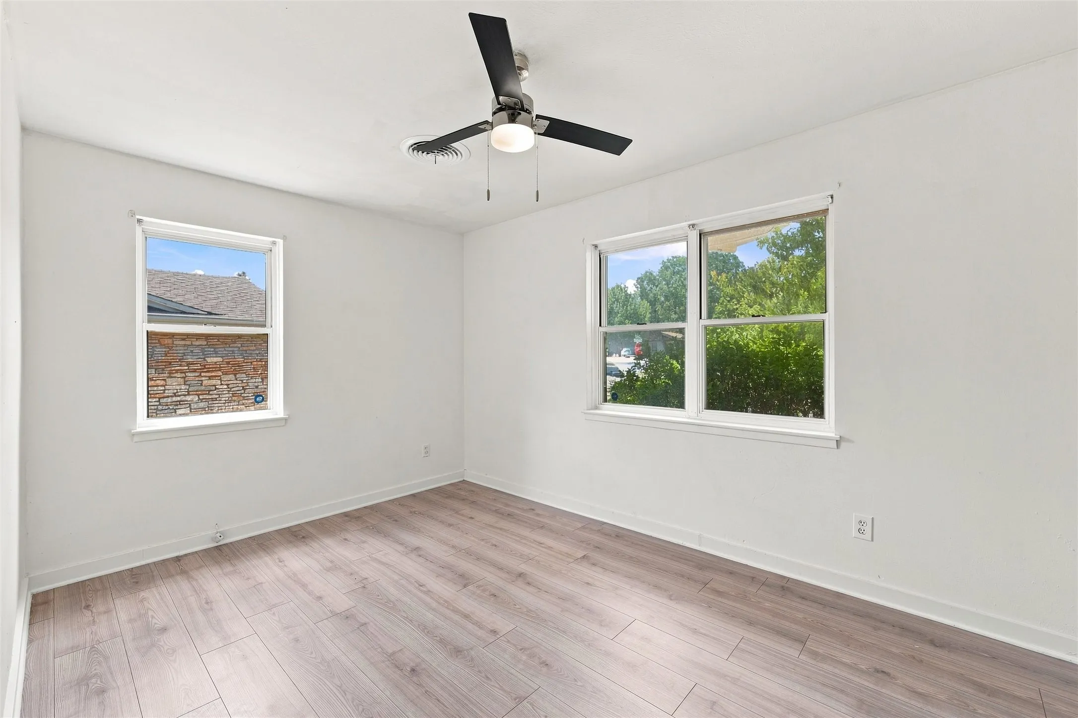 Wood-finish flooring, white walls, two windows, and a ceiling fan with integrated lighting